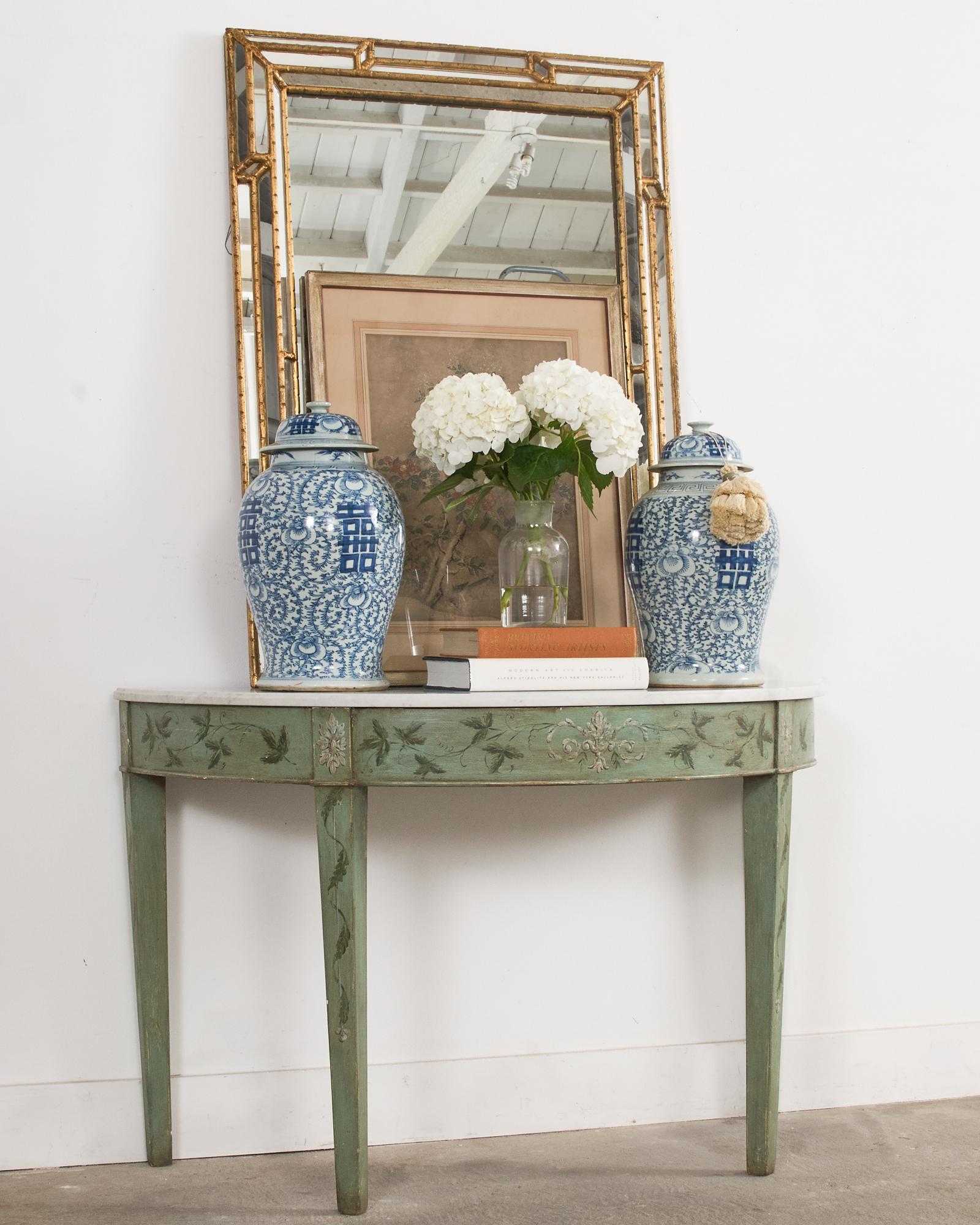 Fantastic pair of mint green painted demi-lune console tables featuring  dramatic Carrara marble tops. Crafted from pine and made in the Swedish Gustavian taste with hand-painted floral and foliate reserves on the apron and legs. The Carrara marble