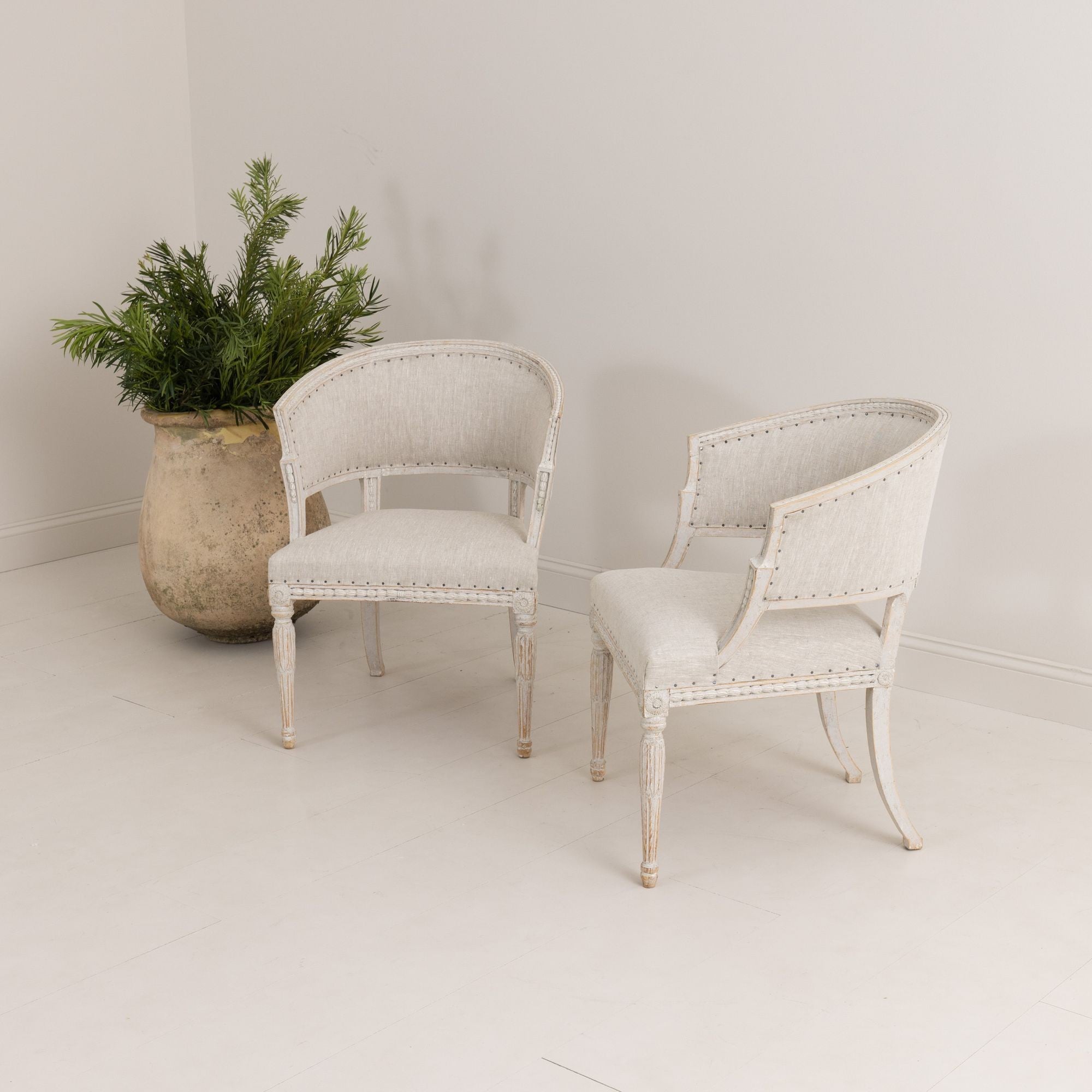 A pair of Swedish chairs with classic sulla barrel backs in the Gustavian style with plaster decorative details, newly upholstered in linen. Beautifully carved bell flowers around the backs of the chairs and on the seat frame, rosettes on the corner