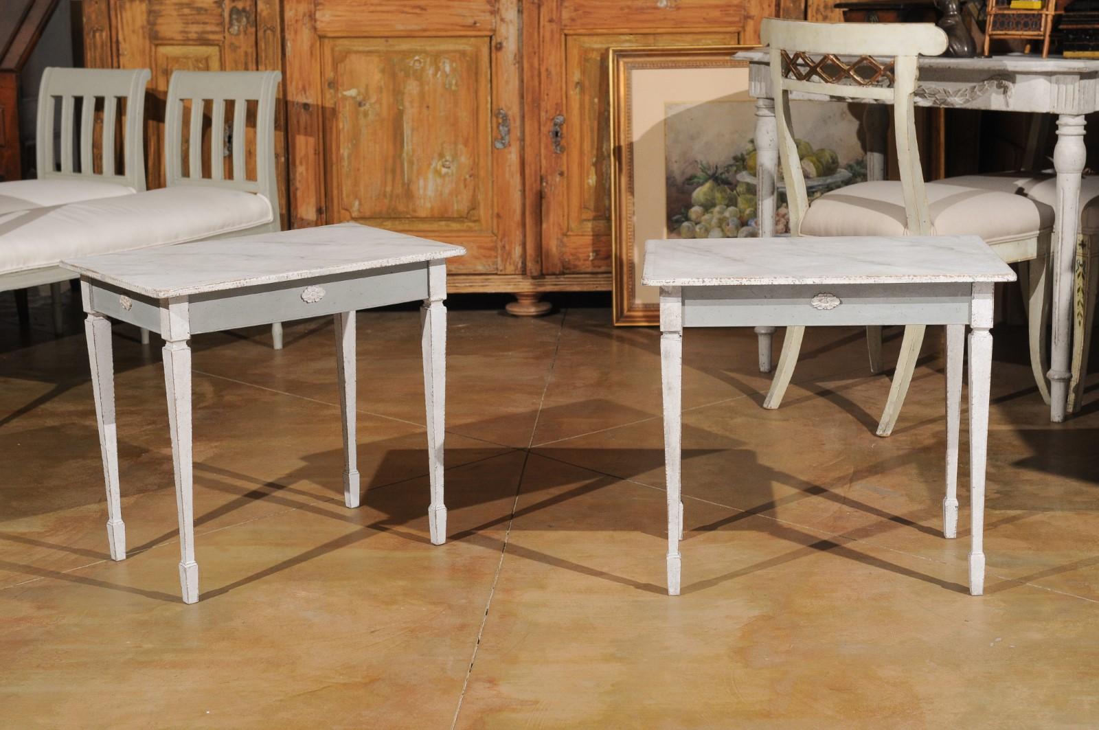 A pair of Swedish Gustavian style small side tables from the 20th century, with faux marble tops and carved rosettes. Created in Sweden during the 20th century, each of this pair of painted side tables features a rectangular marbleized top sitting