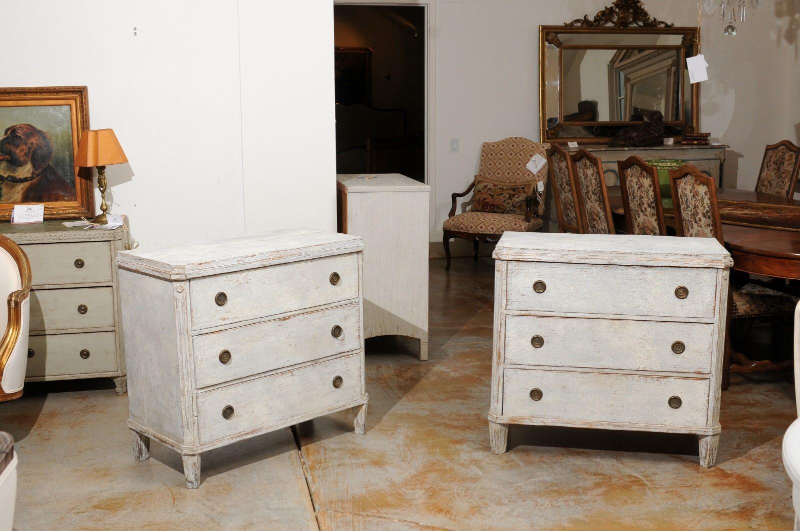 A pair of Swedish Gustavian style painted wood chests from the 19th century, with three drawers and fluted side posts. Created in Sweden during the 19th century, each of this pair of chests features a rectangular raised top with canted corners in