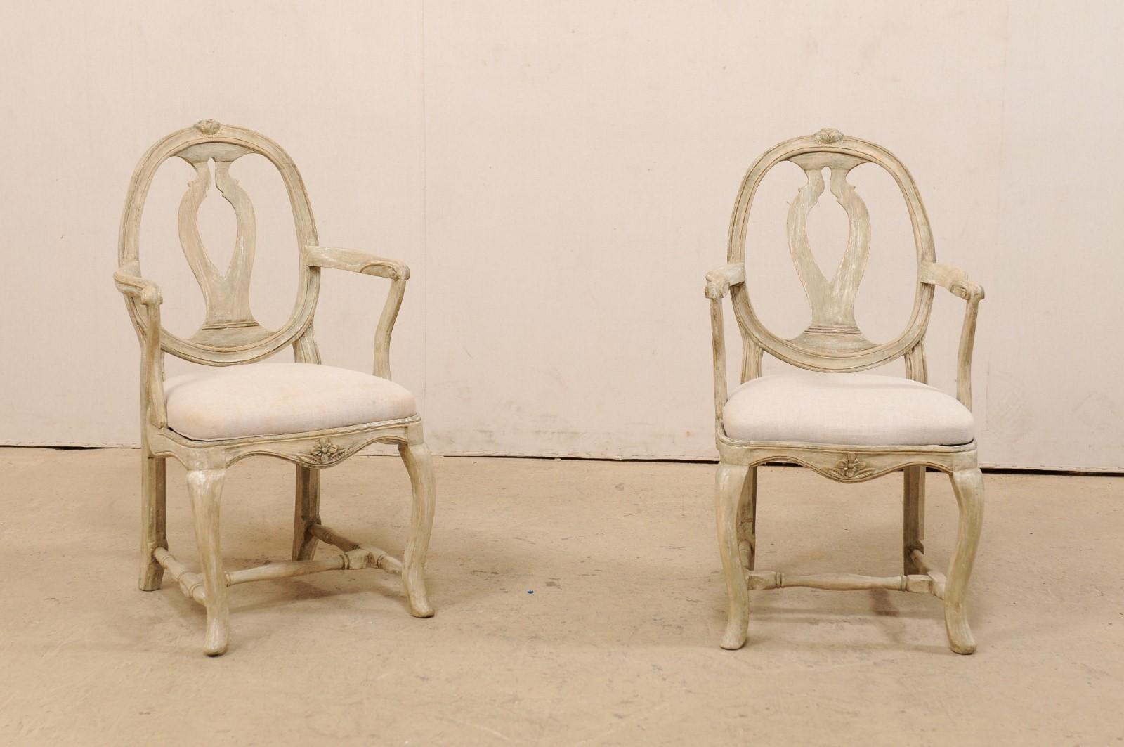 A pair of Swedish Gustavian carved-wood armchairs from the early 19th century. This splendid pair of antique 'Svenska Modellen' (meaning Swedish Model) armchairs from Sweden feature the open, rounded framed backs with wavy, pierced splat-back,