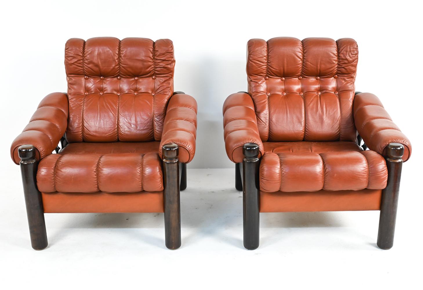 A fabulous pair of Scandinavian modern lounge chairs in stitched and tufted brick leather with stained wood frames. With unusual turned wood spindle sides. These Swedish mid-century chairs are in the manner of Arne Norell or Percival Lafer, with no
