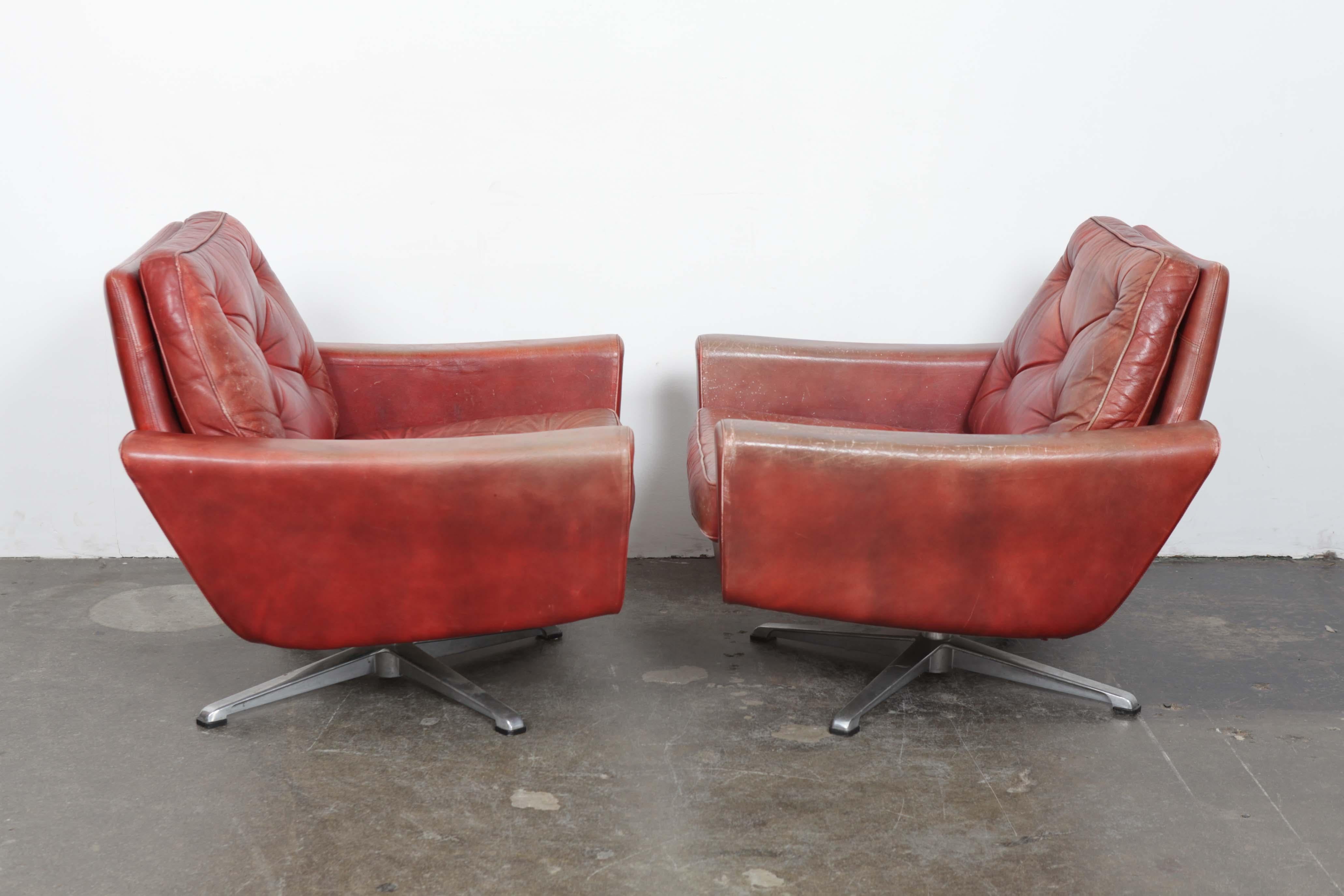 Pair of 1960s low swivel lounge chairs in original red tufted leather with incredible patina, made in Sweden. The swivel bases are a very solid metal base. The leather shows definite signs of patina/wear/scratches. Back and seat cushion are both
