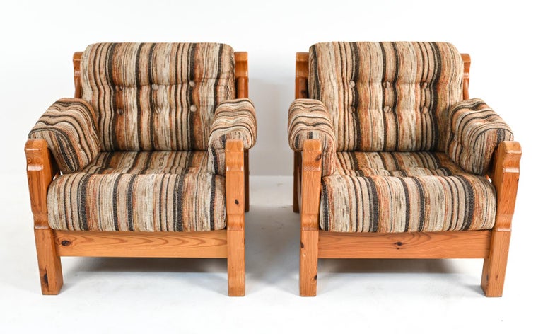 A stylish and highly comfortable pair of Swedish mid-century lounge chairs with rustic-inspired carved pine frames and wool-blend button-tufted upholstery in earth-tone stripes. Featuring slat supports underneath the seat cushions and heavy, sturdy