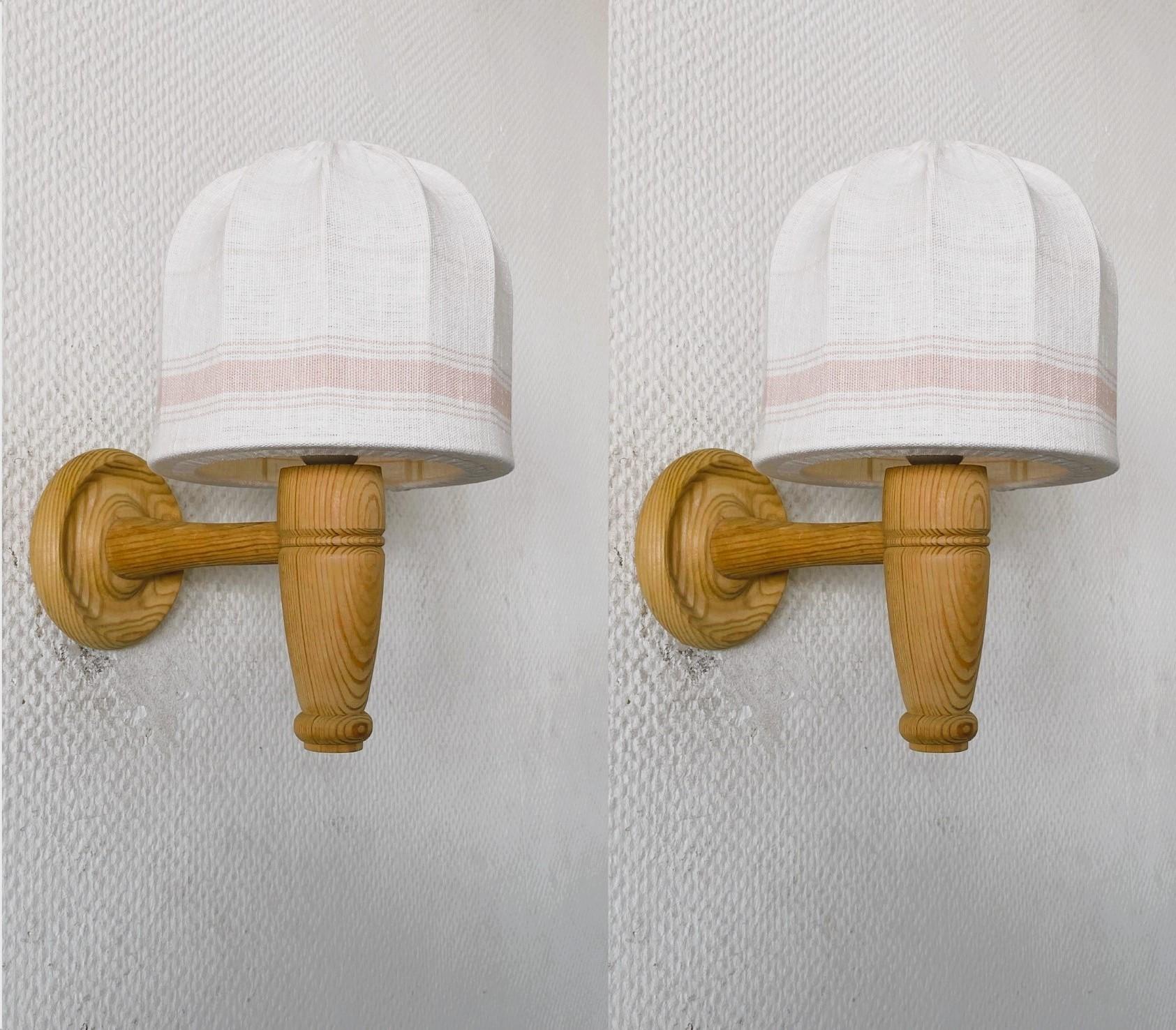 Coppia di applique in legno di pino intagliato a mano, progettate e prodotte in Svezia negli anni '1960. Linee pulite e  design del periodo Scandinavian Modern, con bellissimi paralumi in lino fatti a mano. Entrambe le applique sono in ottime