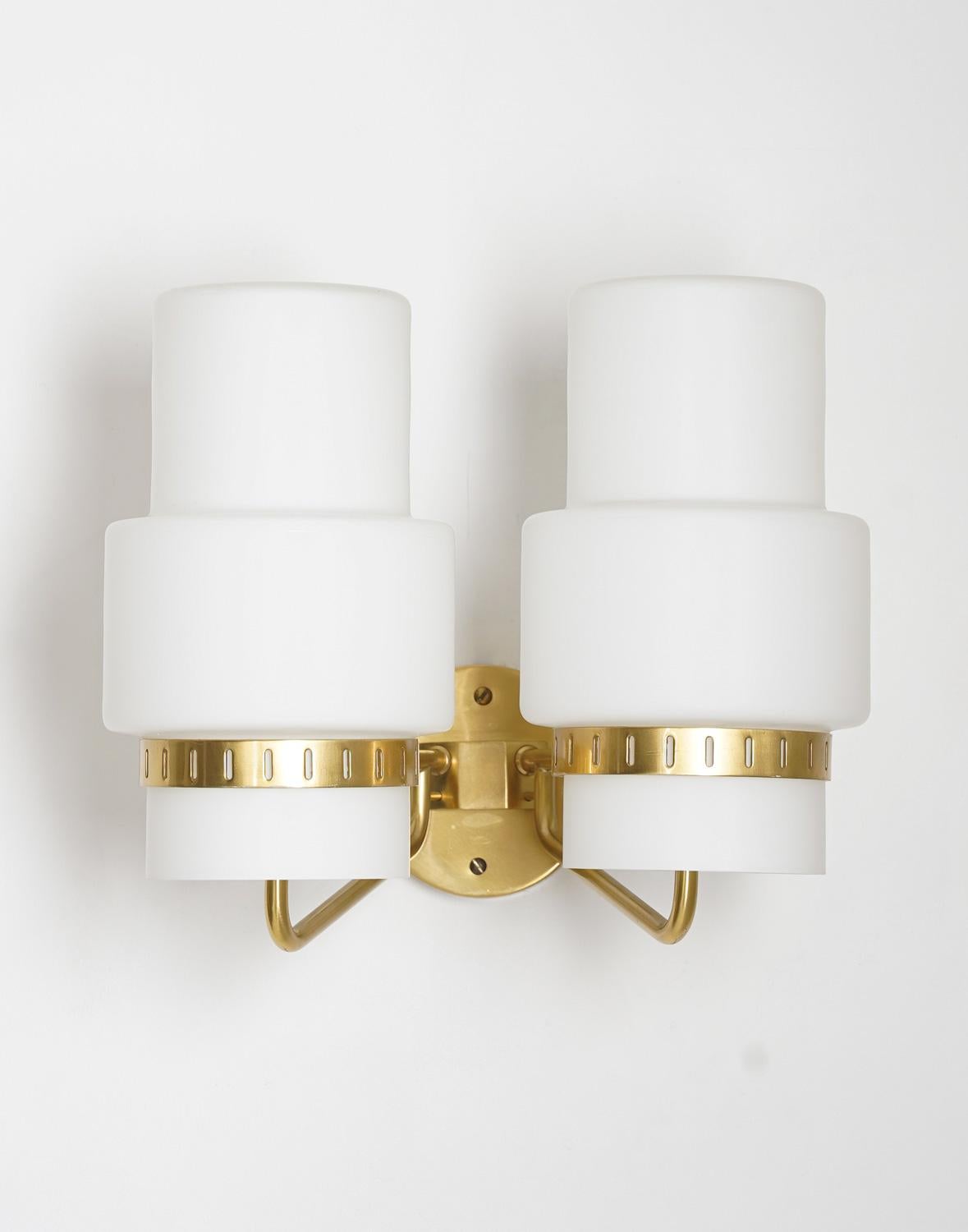 Pair of wall lights manufactured in Sweden circa 1950.
Each lamp features two light sources, hidden by a frosted opaline glass shade. The shades are kept in place by a perforated brass ring. 

Condition: Very good original condition.

 