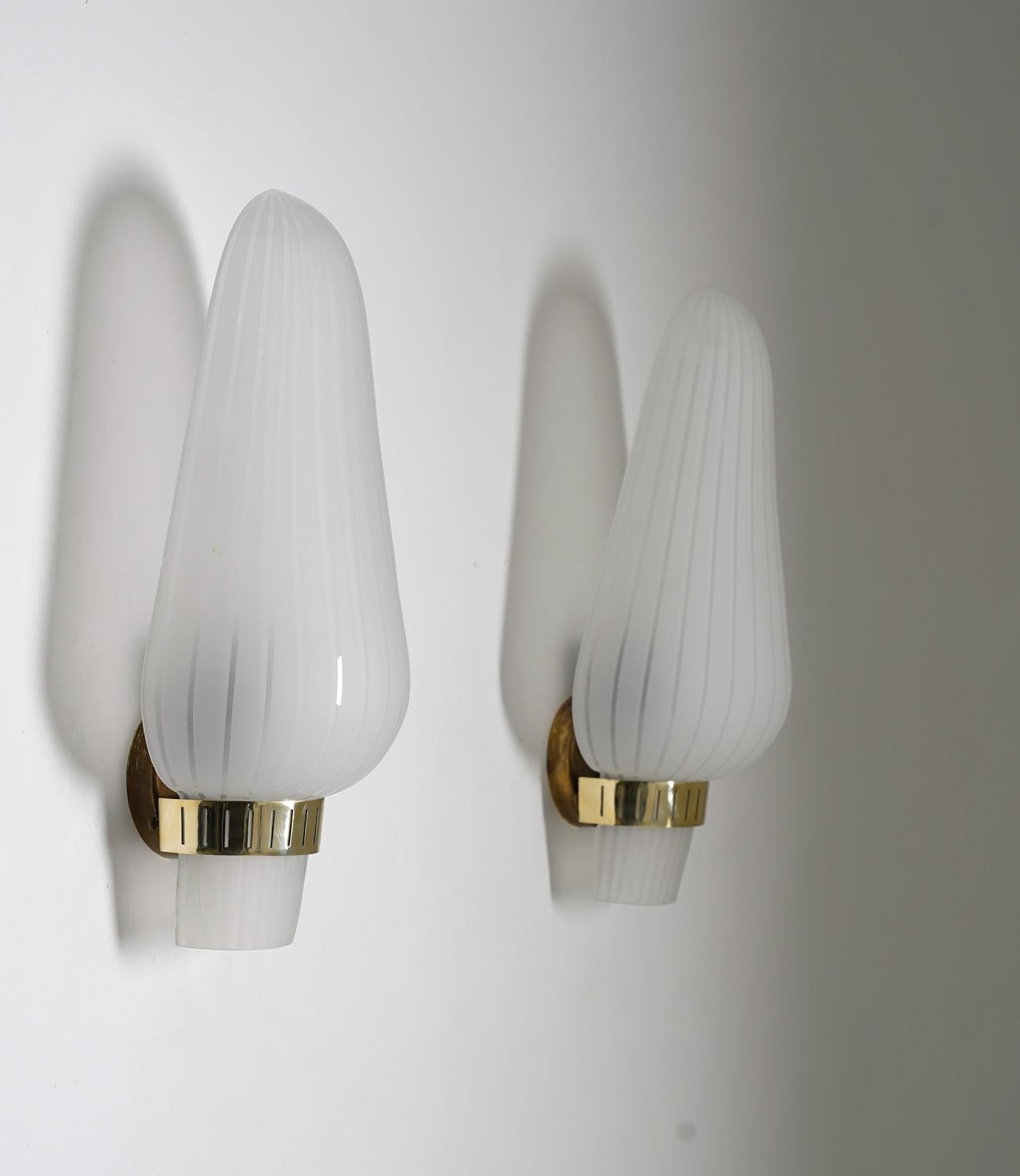 Pair of wall lights/sconces model 8705 by Böhlmarks, 1940s.

Each lamp features one light source, hidden by a large frosted glass shade. The shades are kept in place by a perforated brass holder

Condition: Good condition apart from a few small