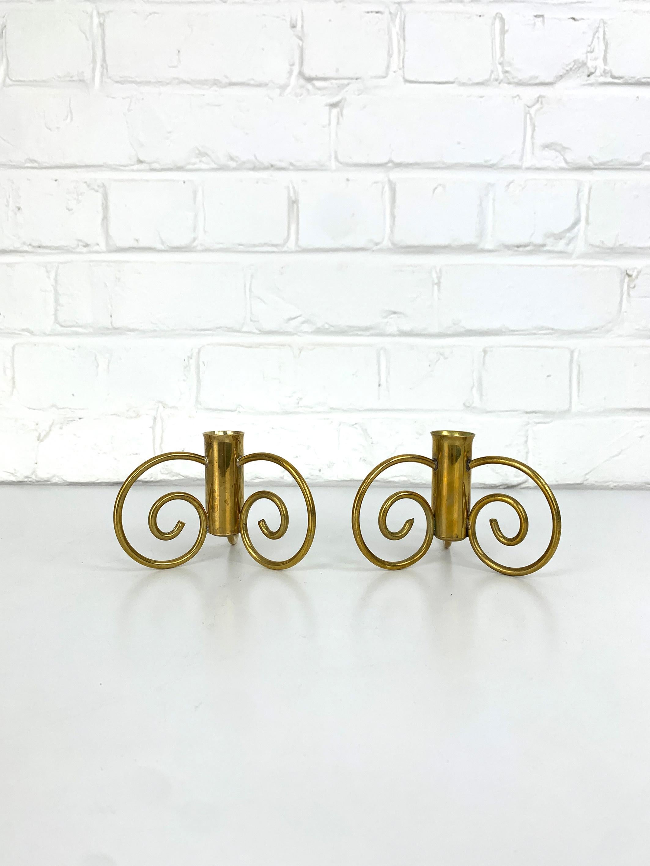 Elegant pair of Swedish Modern candlesticks in solid brass, dating from the 1950s. Each piece features a central tubular element designed to hold one candle. This central element is supported by three finely curved spiral-form feet, set