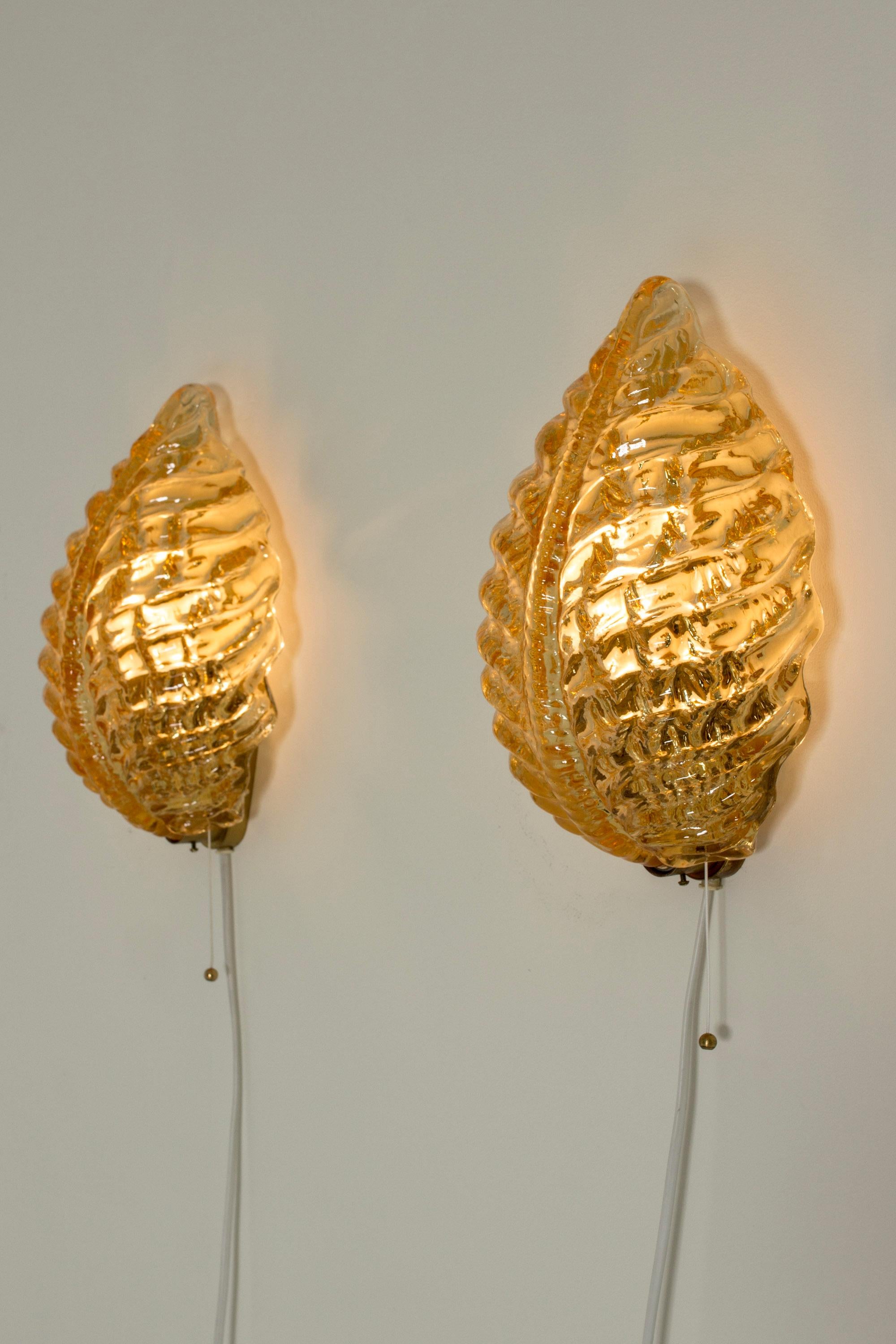 Pair of beautiful Swedish modern wall lamps from Orrefors. Made from glass in a warm amber color, in the form of leaves. Thick glass quality with a fluid look.