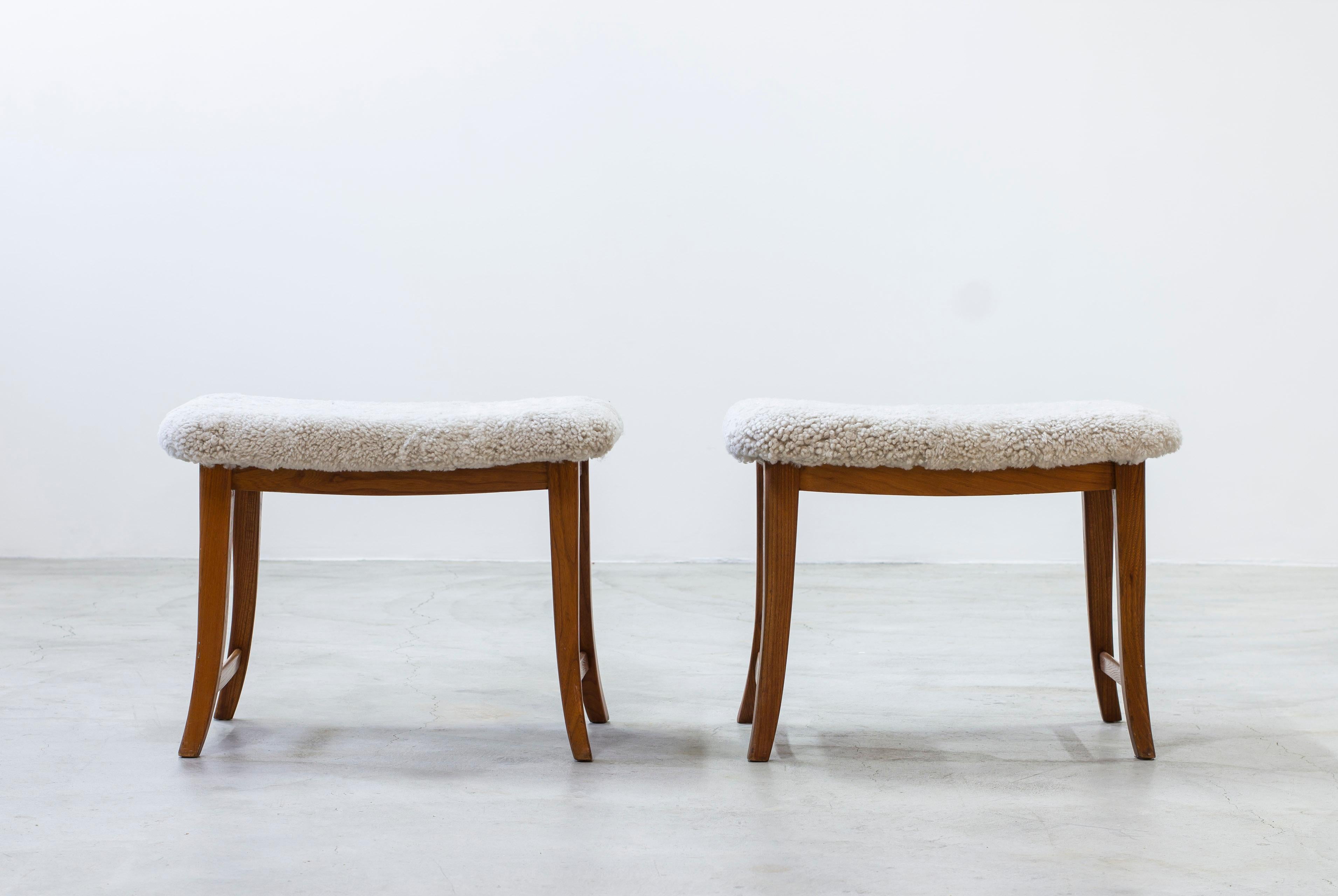 Pair of Swedish modern stools made ca 1940s. Curved and slightly tapered legs in solid elm. New upholstery in sheepskin with white. Works just as well as stools or footrests. Very good vintage condition with light age related wear and patina.