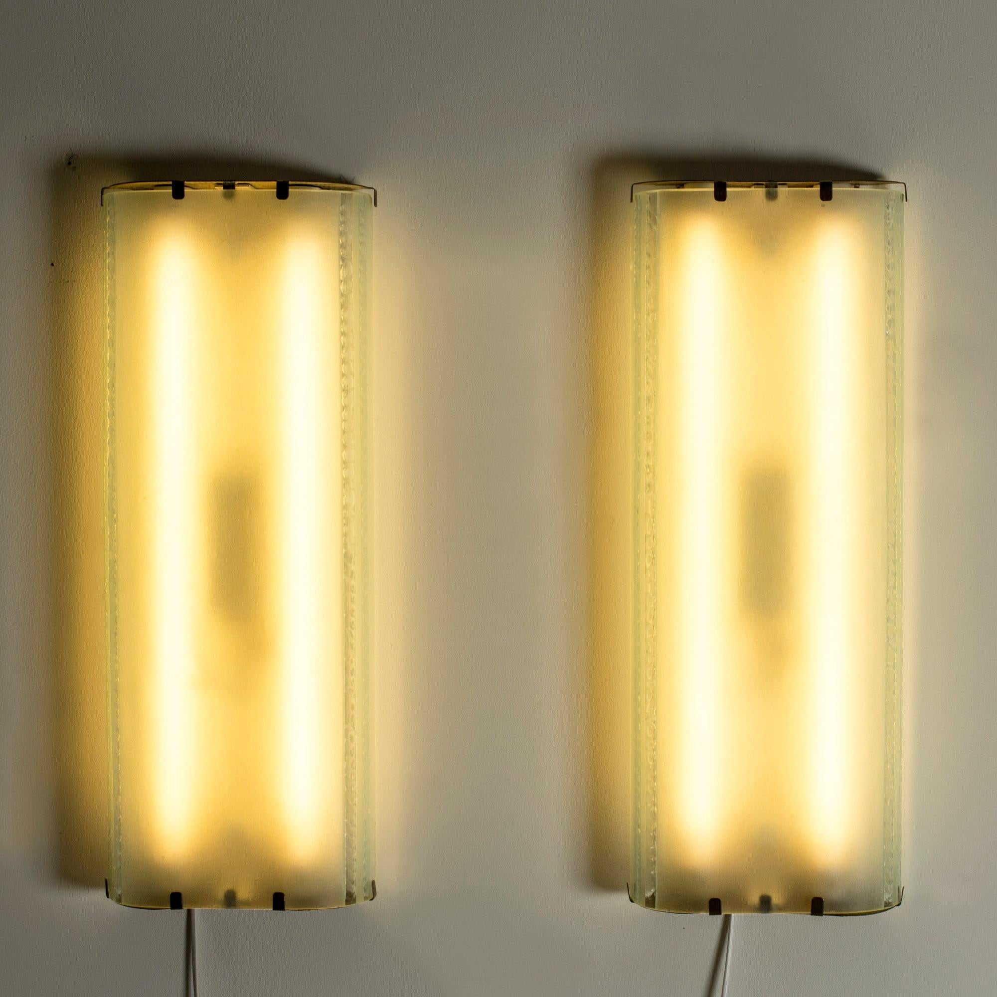 Pair of large, flush mount Swedish Modern wall lights, made from glass and brass. Thick frosted glass with a decorative pattern along the edges. Brass sections hold the glass in place, beautifully decorated in a pattern of perfortated holes.