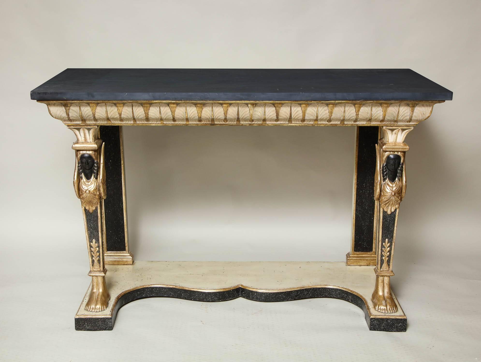 Stunning pair of Art Deco Swedish-Egyptian console tables, having slate tops over silver gilt and white lotus leaf carved molded aprons over caryatid carved herm legs, standing on scalloped platform bases with faux porphyry decoration to the edge,