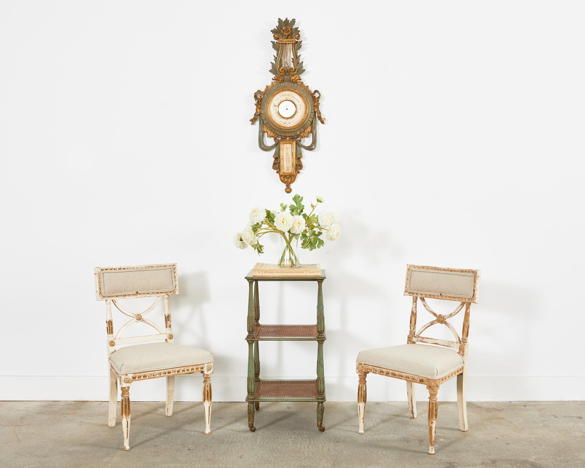 Gorgeous pair of Swedish hall chairs or dining chairs made in the 18th century neoclassical Gustavian taste. The beech frames feature an intentionally distressed painted finish with parcel gilt accents. The klismos style tablet back is supported by