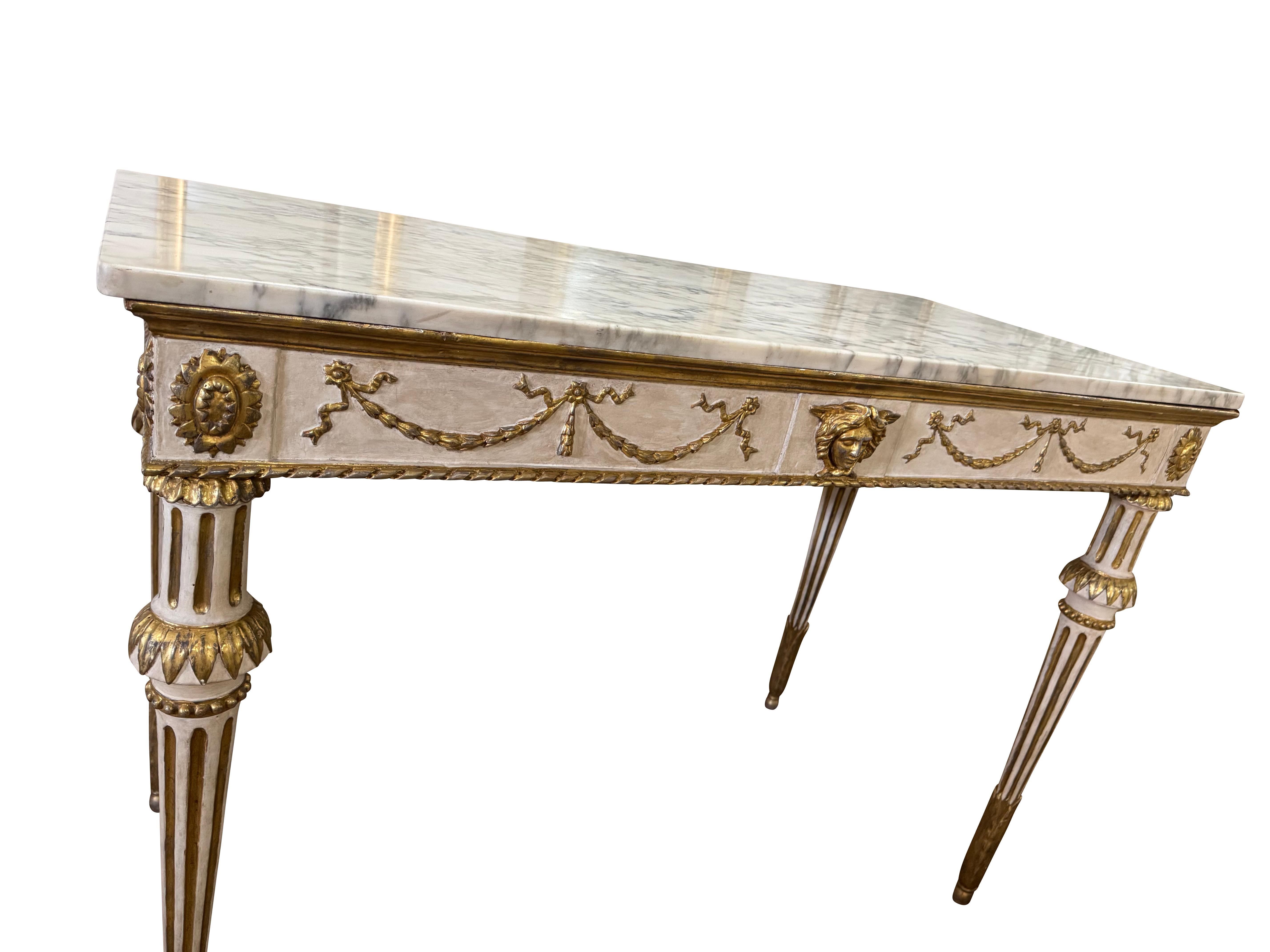 Una coppia eccezionalmente elegante del XIX secolo di  Consolle o tavoli da scrittura neoclassici dipinti e dorati. Il piano di marmo originale poggia su un fregio finemente intagliato e ornato da fasce dorate, rosette e un'impressionante maschera