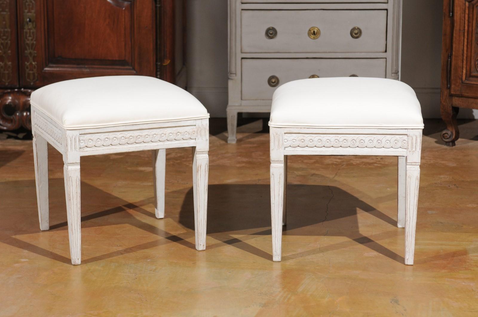 A pair of Swedish neoclassical style painted wood stools from the mid-19th century, with guilloche motifs and new upholstery. Born in Sweden during the first half of the 19th century, each of this pair of stools features a square top recovered with