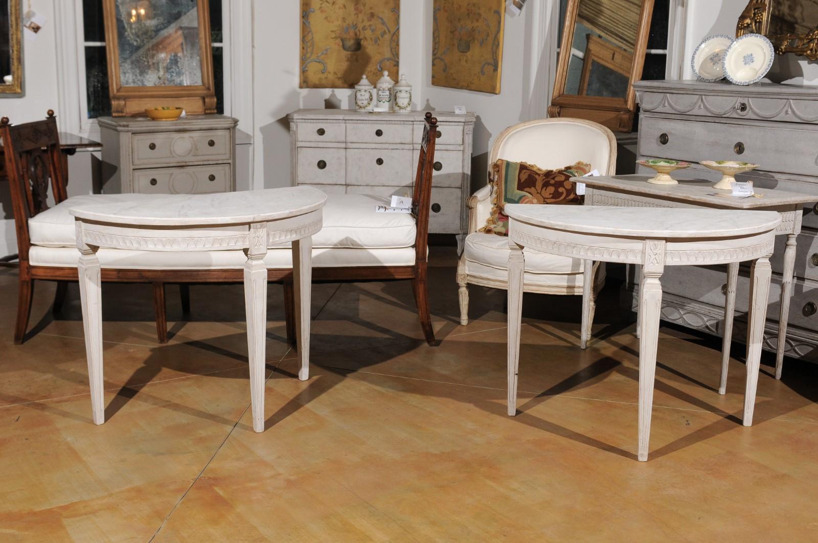 A pair of Swedish neoclassical style painted wood demilune console tables from the late 19th century, with faux-marble tops, waterleaf motifs and carved rosettes. Born in Sweden during the later years of the 19th century, each of these demilunes