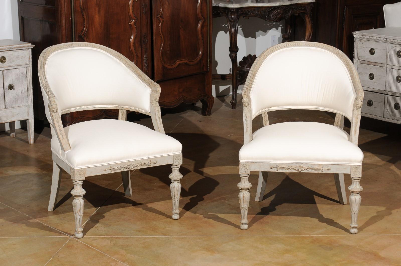 A pair of Swedish 19th century neoclassical style barrel-back chairs from the 19th century, with classical heads, foliage and new upholstery. Born in Sweden during the 19th century, each of this pair of exquisite neoclassical style armchairs