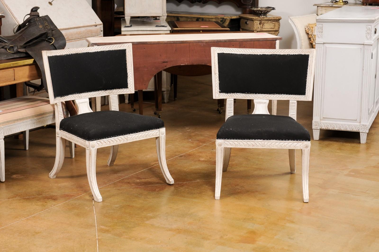 Ein Paar schwedische Klismos Beistellstühle im neoklassizistischen Stil aus lackiertem Holz aus dem 20. Jahrhundert, mit geschnitztem Dekor, Rosetten, Säbelbeinen, niedrigen Sitzen und einfacher schwarzer Polsterung. Dieses Paar Klismos-Stühle wurde