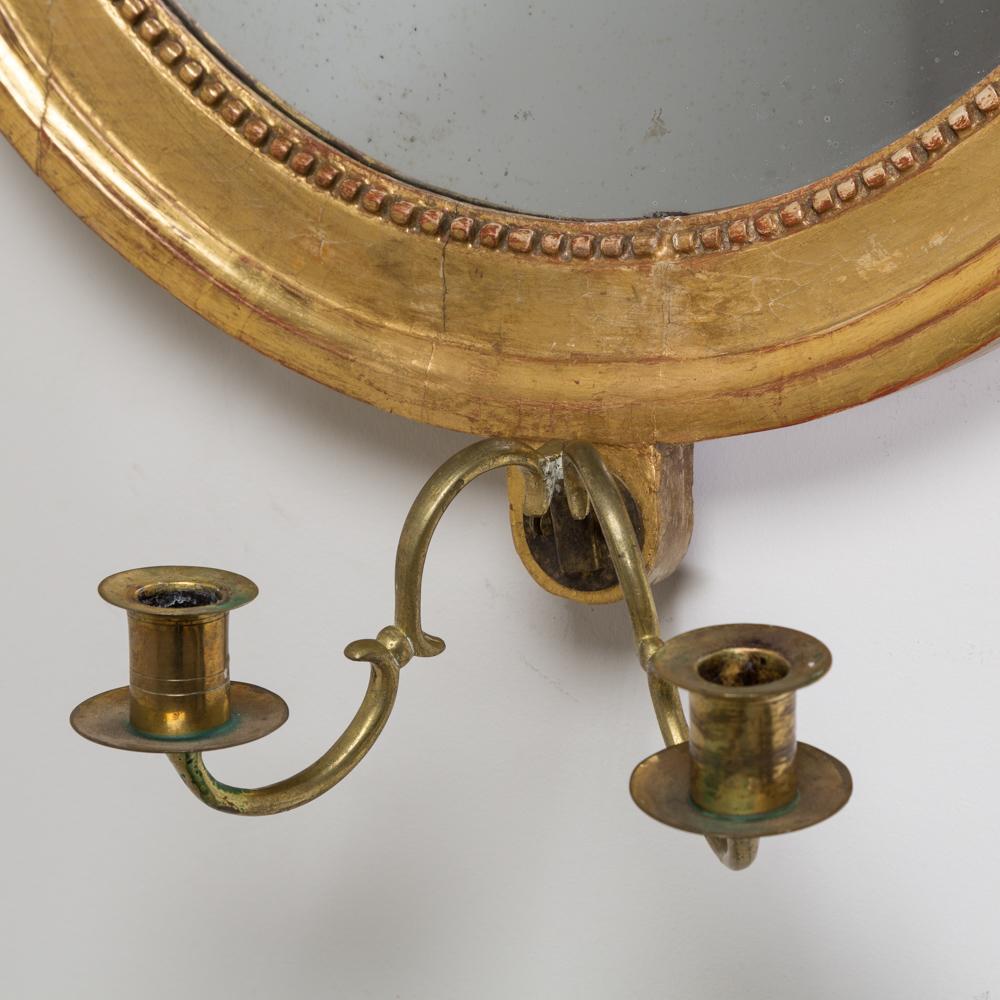 A pair of Swedish Gustavian oval giltwood mirrors with gilt ribbon and foliage detail to the top and hand carved beading surrounding the mirror plate which have been gilded and carefully burnished to show the red underneath. The back of the mirrors