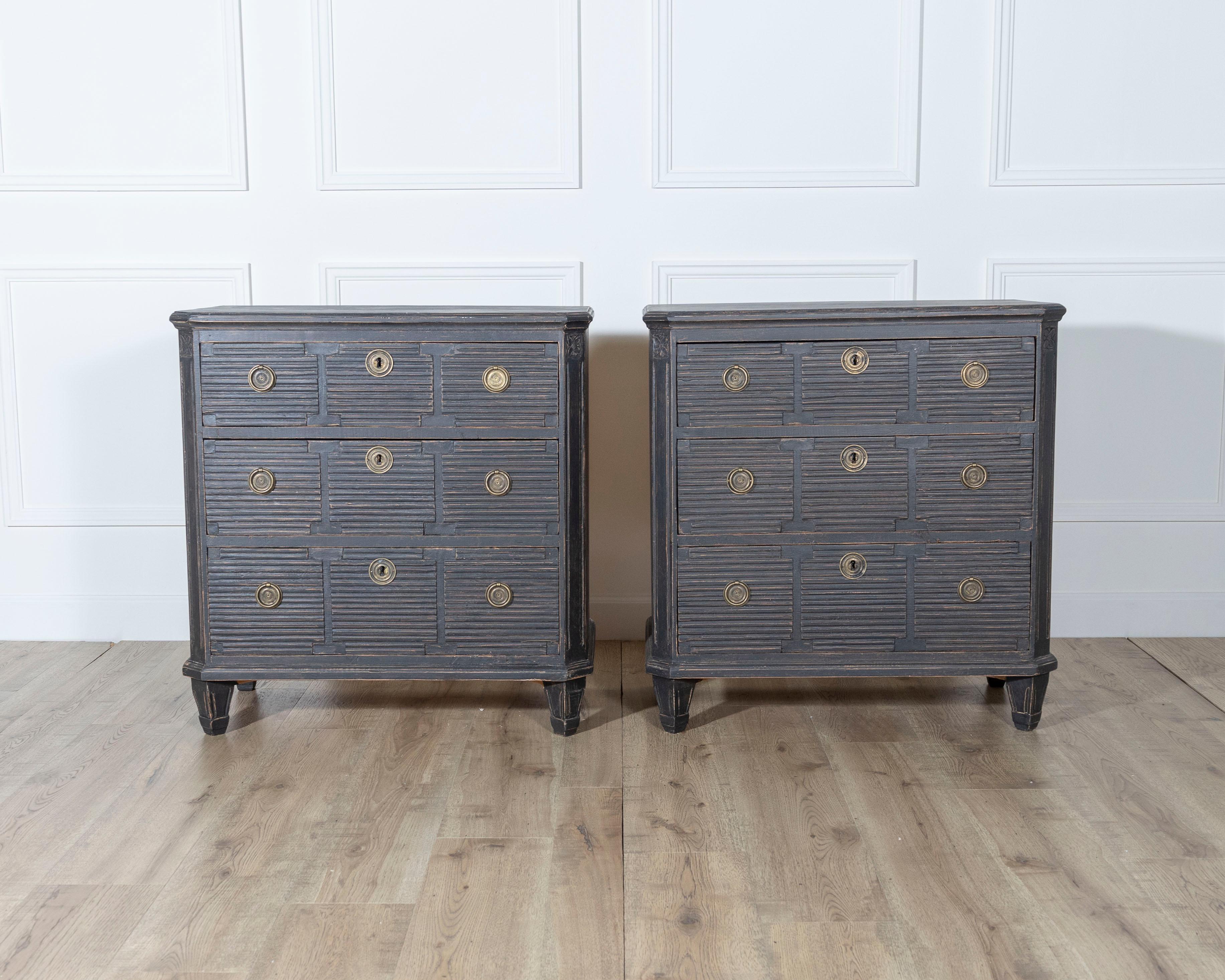 A distinctive pair of Swedish chests of drawers, likely crafted in the early 20th century, featuring richly textured façades with horizontal fluting across each drawer front. Painted in a muted charcoal-black tone with a beautifully worn patina, the