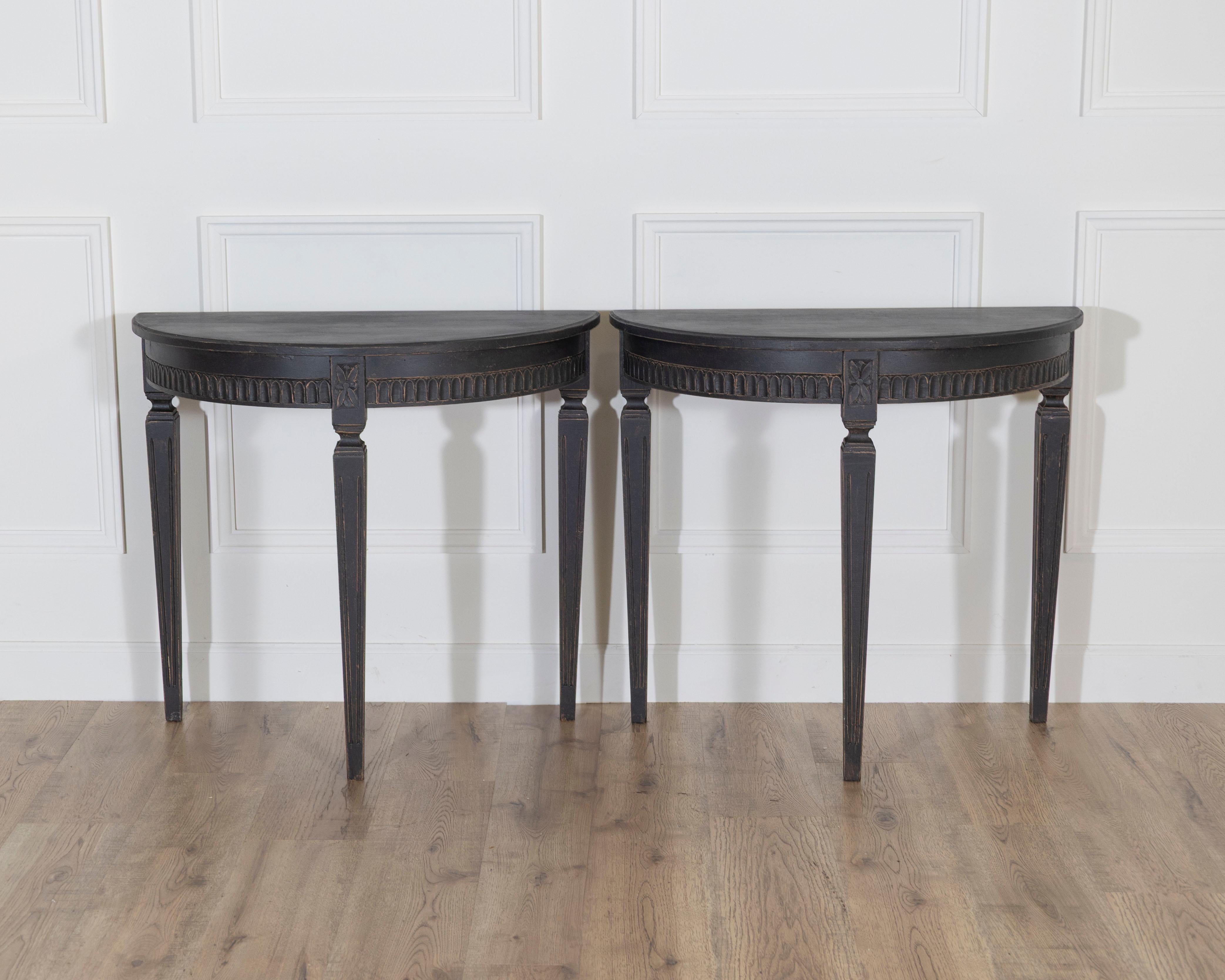 A striking pair of Swedish demi-lune consoles from circa 1880, painted in a deep, dramatic tone that lends a sense of gravity and sophistication to their neoclassical form. Each console is designed with a semi-circular top supported by four elegant