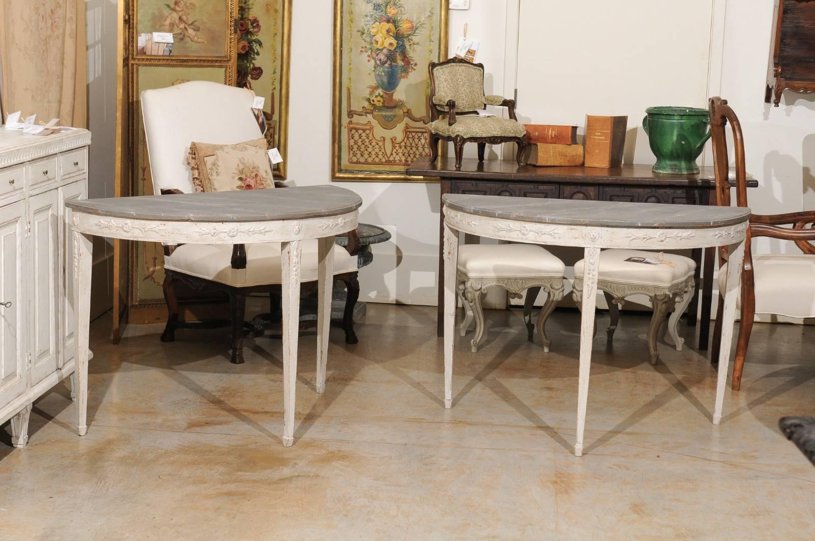 A pair of Swedish neoclassical period painted wood demilune console tables from the early 19th century with marbleized tops, carved aprons and tapered legs. Each of this pair of Swedish demilune features a grey veined faux-marble semi-circular top