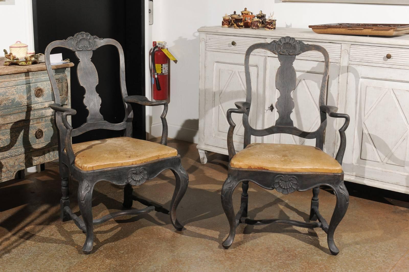 A pair of Swedish Rococo style painted wood armchairs from the late 19th century, with antique leather covered seats, carved splats, cabriole legs and cross stretchers. Each of this pair of Swedish armchairs features a beautifully pierced back with