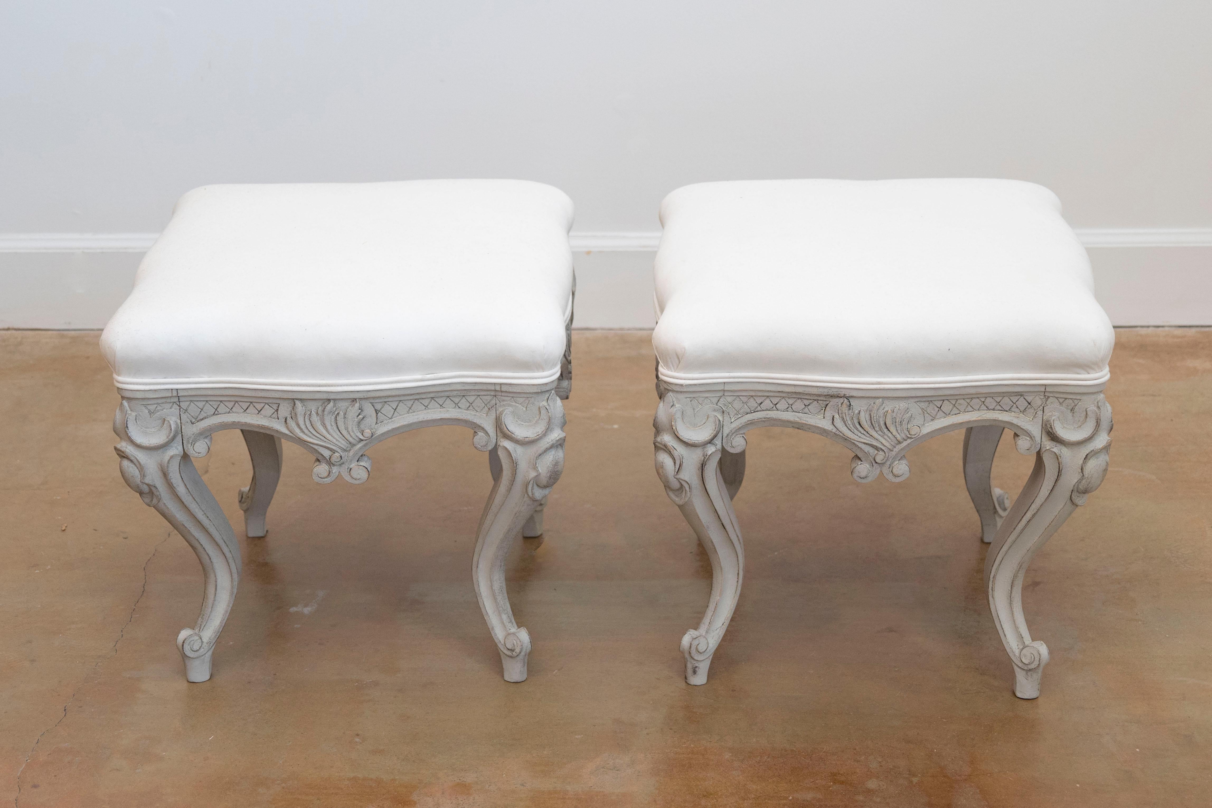 A pair of Swedish Rococo style painted stools from the late 19th century with richly carved décor, cabriole legs and newly upholstered seats. Each of this pair of Scandinavian Rococo style stools features a square seat reupholstered in a double welt