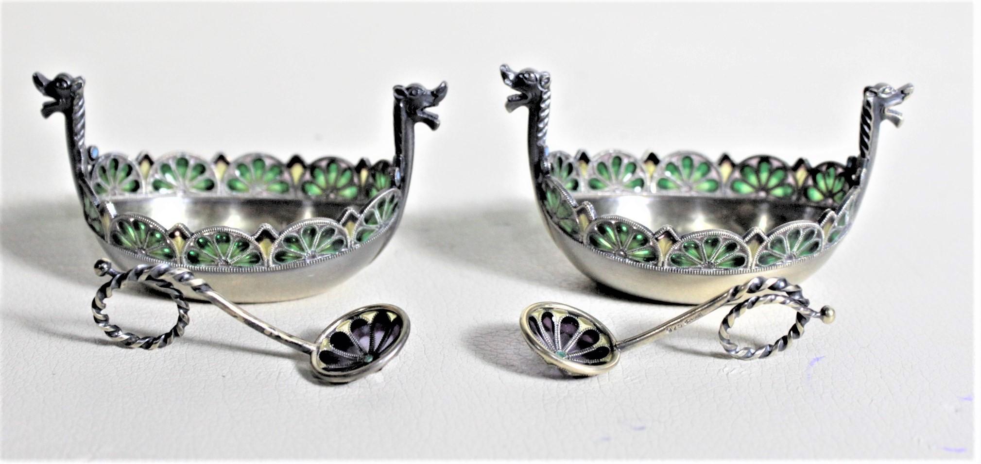 This pair of sterling and enameled salt cellars and spoons was made in Sweden in circa 1925 in the Modernist style. The pair of salt cellars are figural Viking longboats which have been ornately crafted with dragon heads on either end and which have