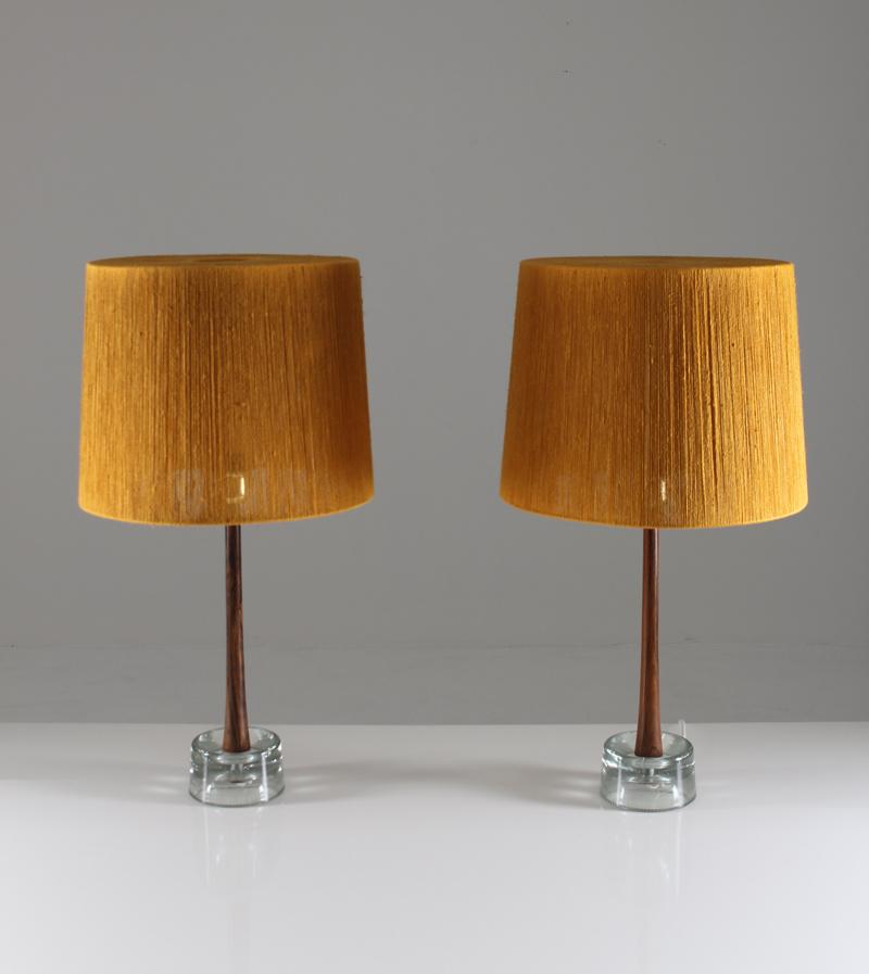 This rare set of two midcentury table lamps was manufactured in the 1960s by Stilarmatur Tranås in Sweden. The lamps consist of a clear glass foot, underneath a stem in beautiful rosewood. They come with gorgeous vintage shades in gold-yellow