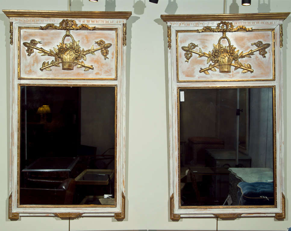 Pair of Swedish wall console or pier mirrors. Each having a Painted And Parcel Gilt finish with a clean center mirror in a wooden distressed gilt and painted frame. The top having a finely carved basket of flowers with intertwining arrows.
