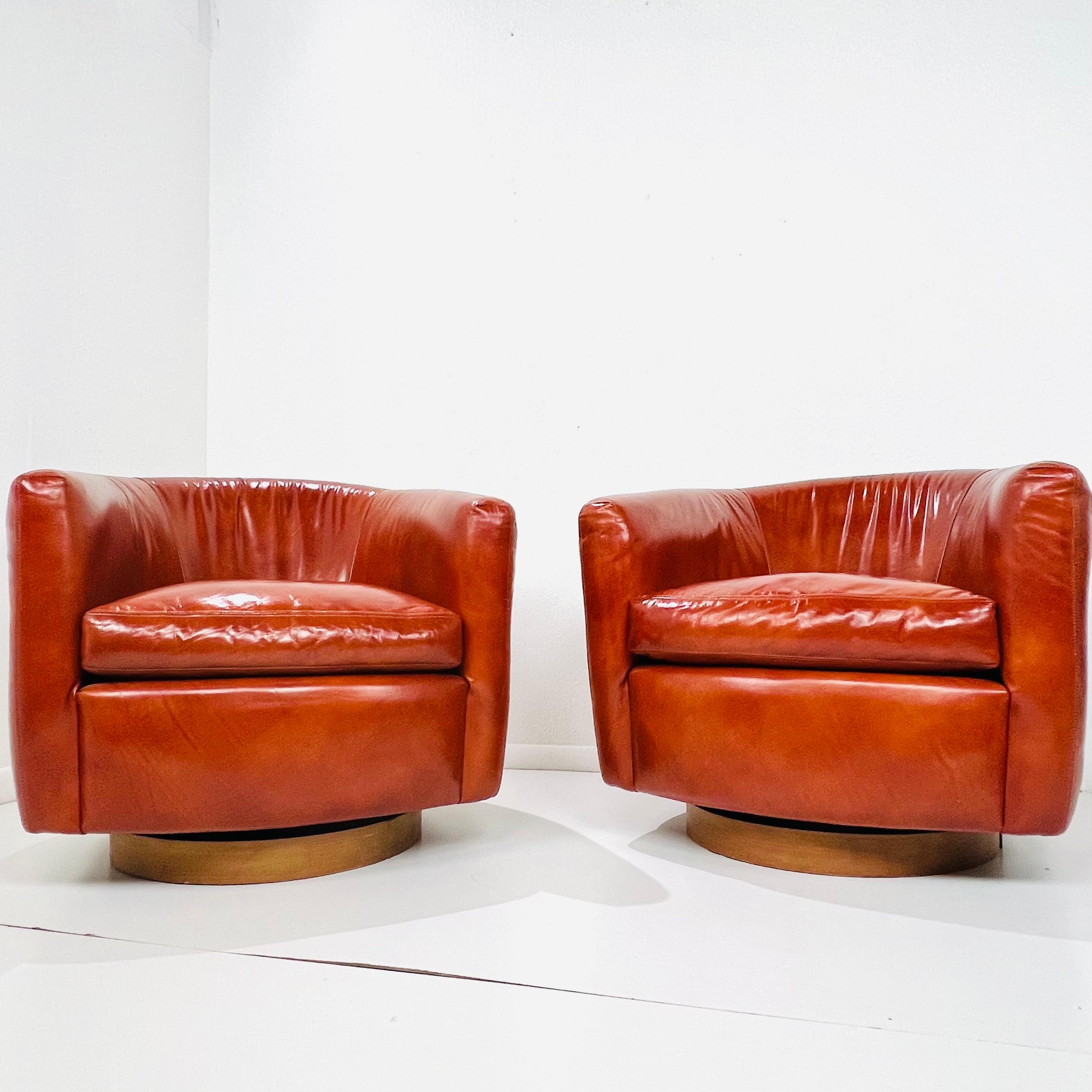 Pair of classic tub chairs designed by Milo Baughman for Thayer Coggin, with walnut bases that swivel and rock. Leather upholstery with fabric backs. Very good condition with very minimal wear (hardly used!). Both chairs retain Thayer Coggin tags,