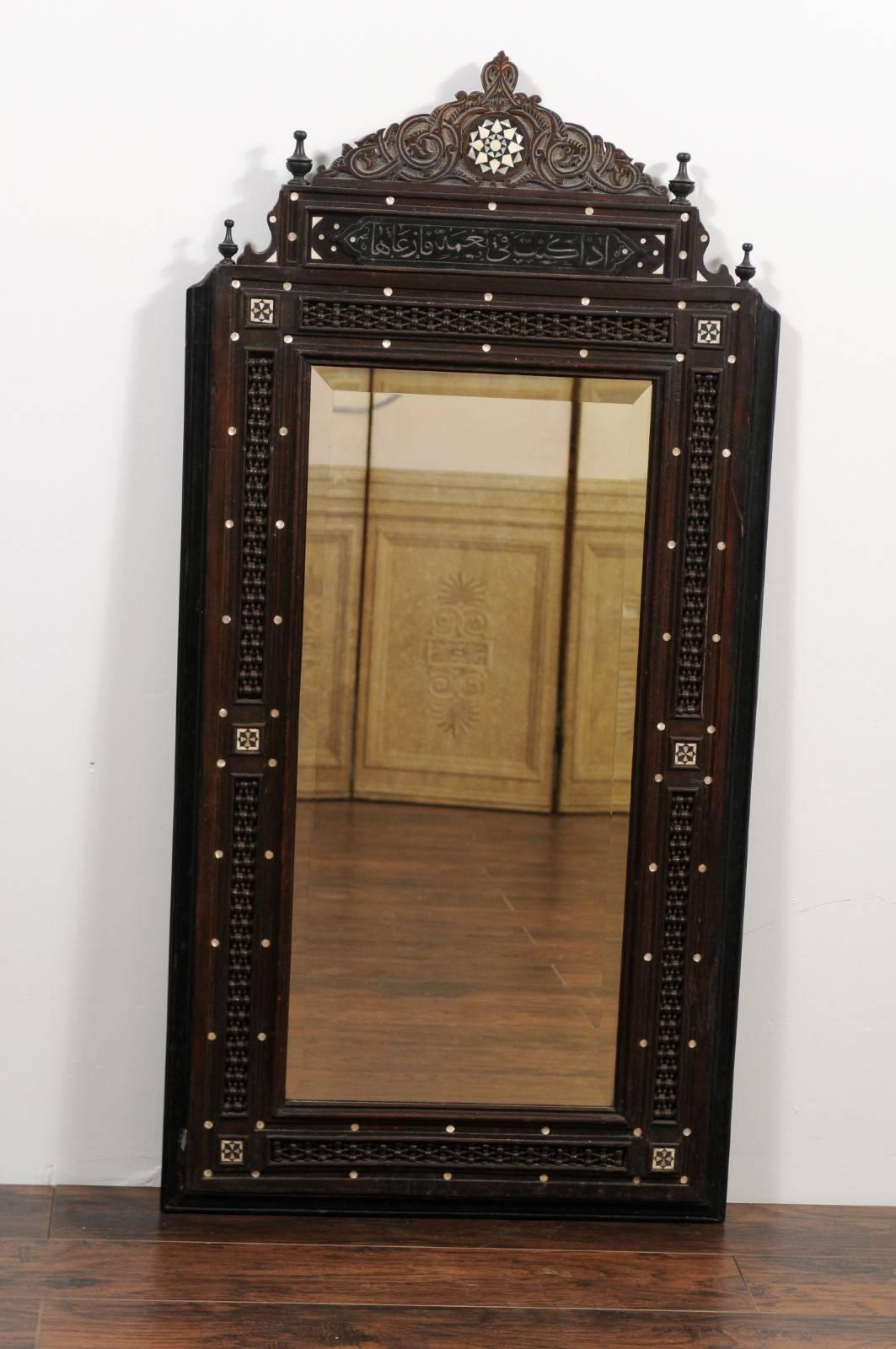 A pair of tall hand-carved Syrian mirrors with mother-of-pearl inlay and ebonized wood accents from the early 20th century. Each of this pair of Syrian mirrors features an exquisite frame. The triangular crest is adorned with a central star-shaped