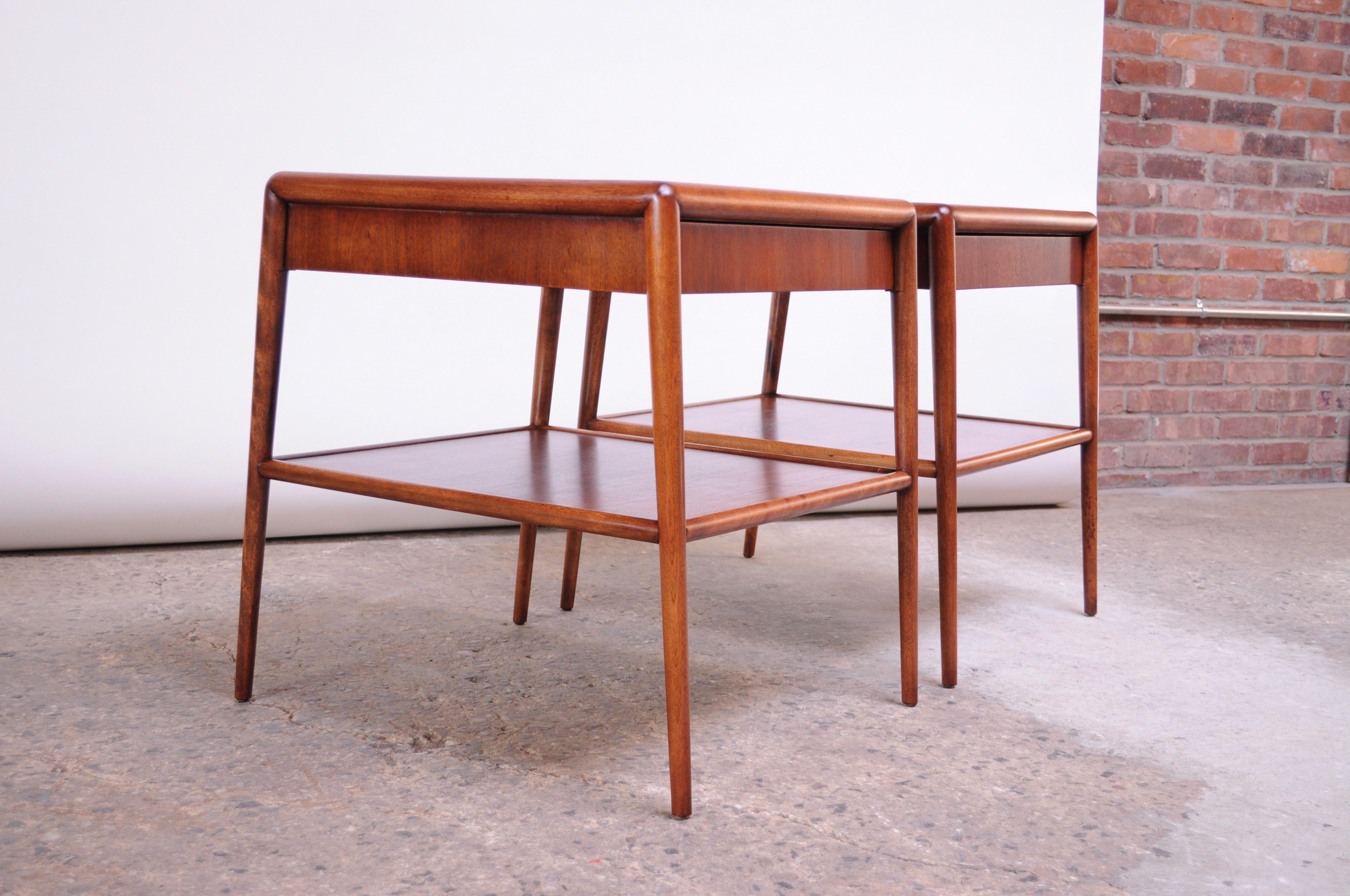 These scarce walnut end tables were designed by Robsjohn-Gibbings for Widdicomb in the 1950s and feature two tiers and a single drawer. Superior craftsmanship and clean, minimal design. Both end tables retain the Widdicomb / T.H. Robsjohn-Gibbings