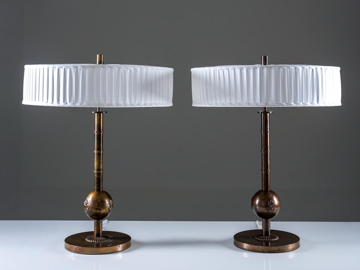 Elegante par de lámparas de mesa de Arvid Böhlmarks Lampfabrik, fabricadas en latón oxidado con un tono cálido y envejecido. Cada lámpara presenta un tallo escultural con sutiles crestas decorativas y un centro esférico ornamentado con relieves