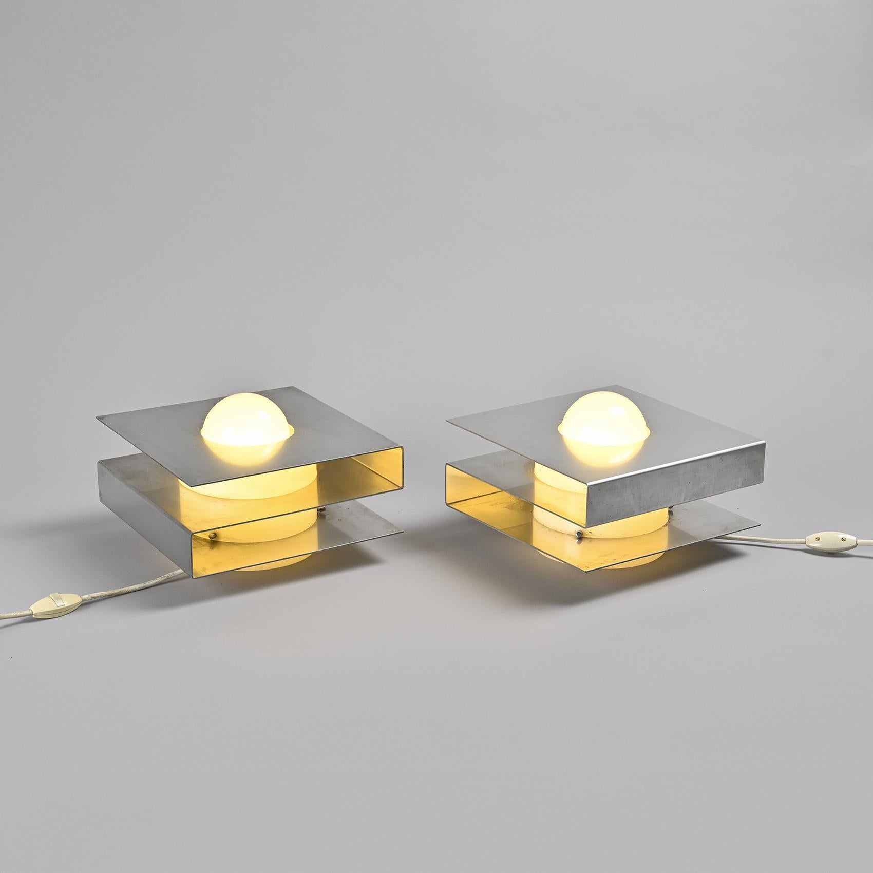 
Pair of table lamps designed by Guy Bertrand in the late 1960s.

Each lamp features a folded aluminium sheet forming a cubic, architectural volume that encloses a plexiglass reflector, producing a soft and even light. The dialogue between the