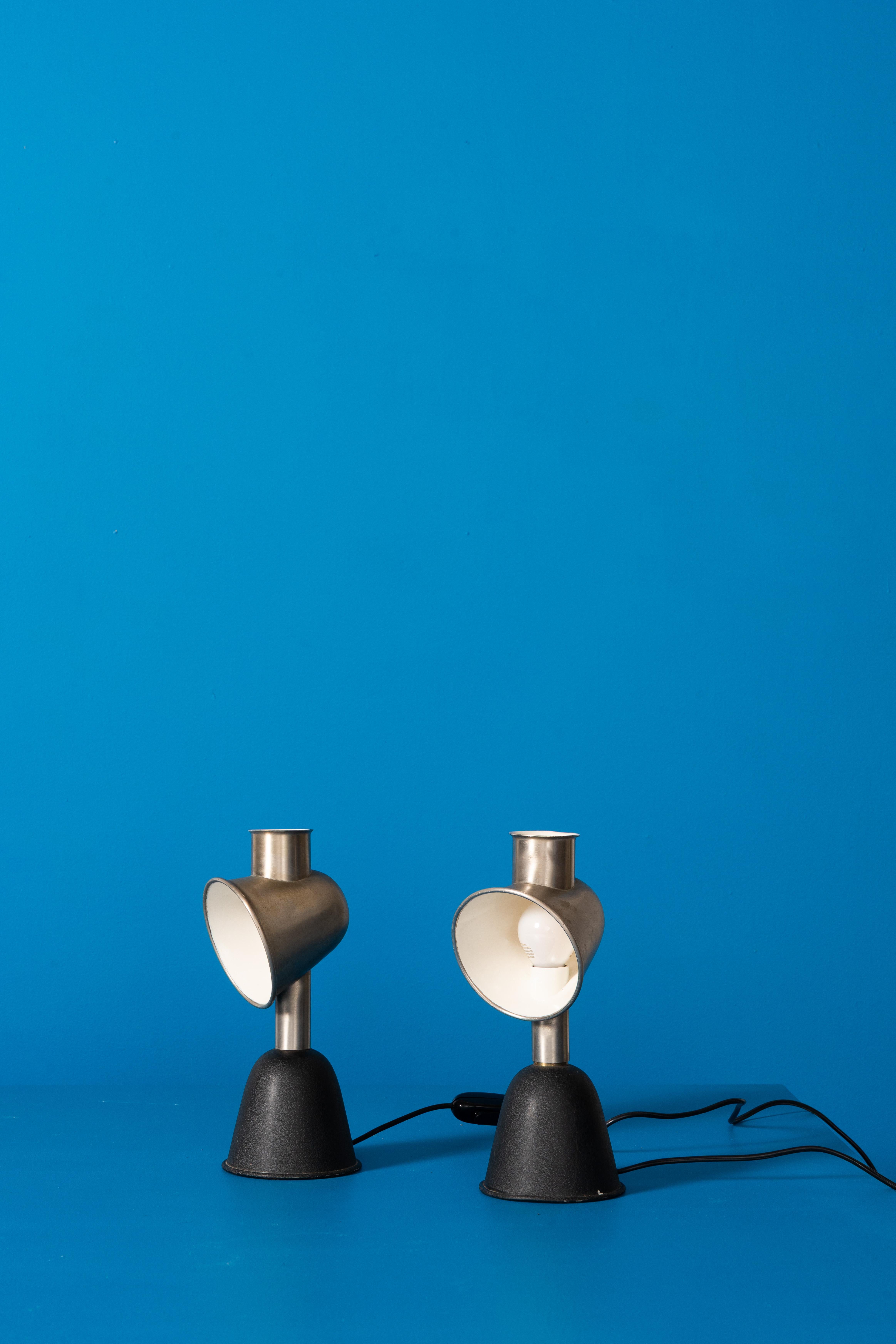 This set of lamps are built around a brushed metal upper shade with a flared profile that directs light forward while softening glare. The inner reflector, finished in white, enhances brightness and creates a clean, diffused glow.

The lamps rest on