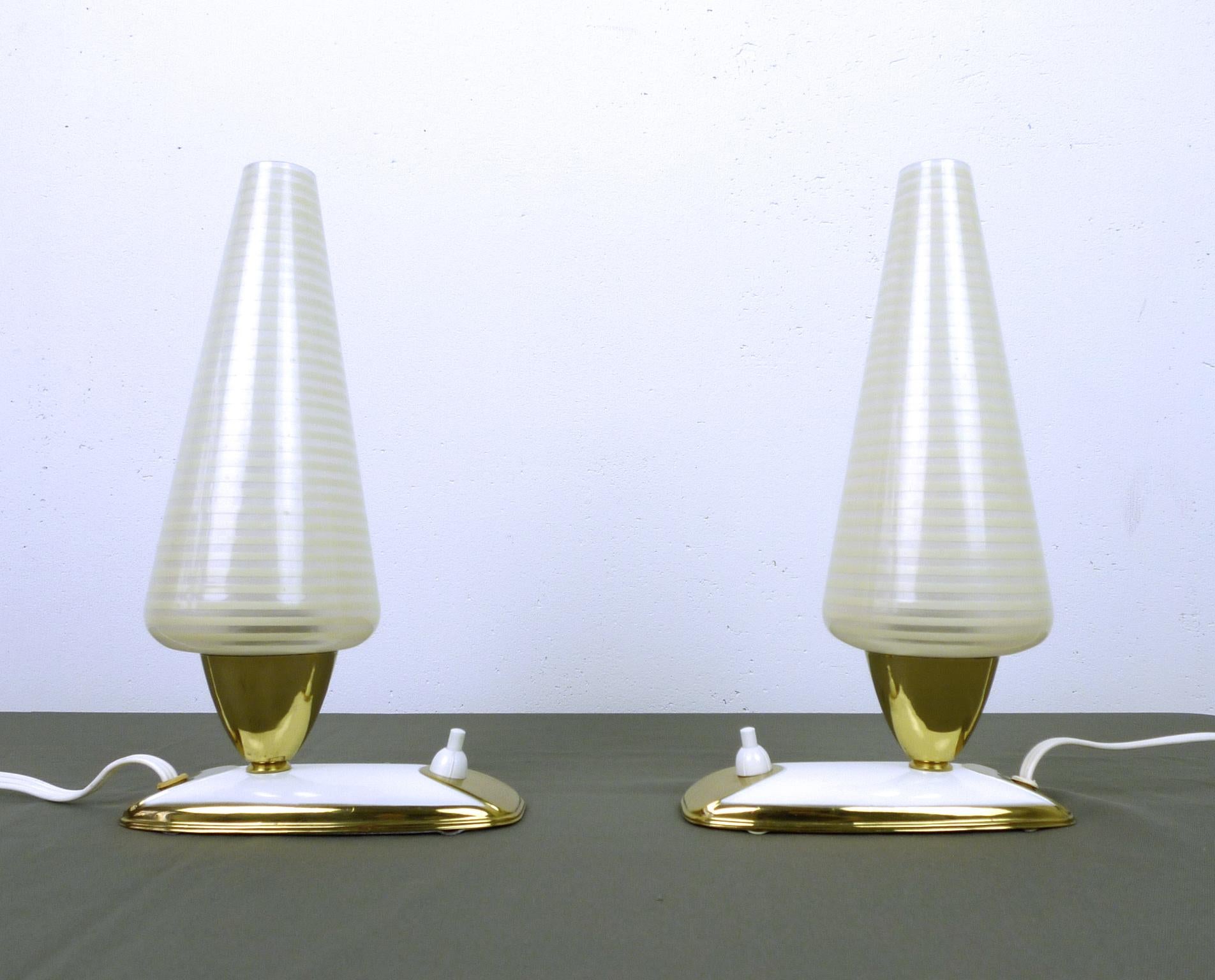 Pair of German table lamps from the 1950s. Both lights have a narrow white stand with brass elements and a pressure switch on the front. The slender striped glass diffusers are stuck on E 14 lamp sockets. The table lamps are in very good condition.