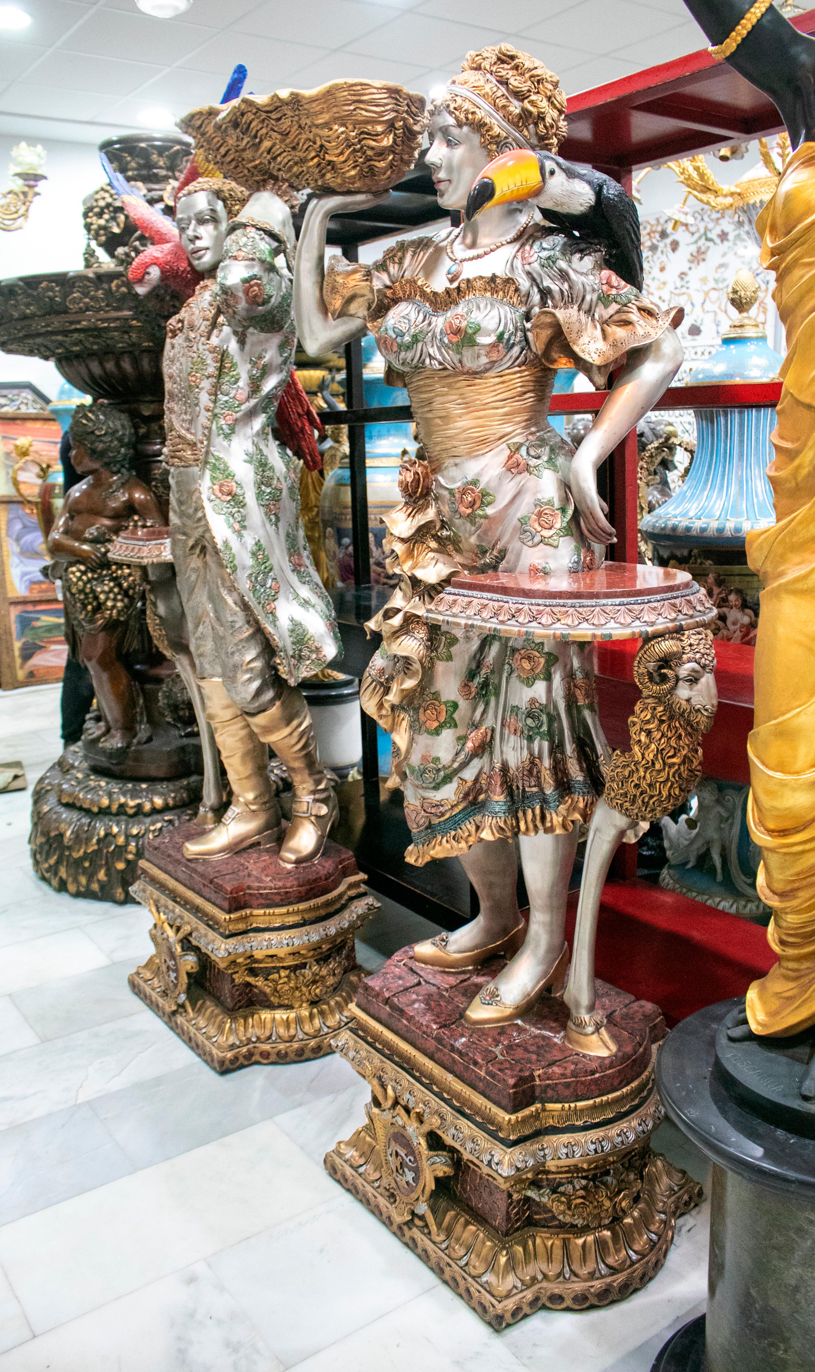Pair of tall bronze life-size painted Venetian sculptures with birds and conchs, standing on pedestals.