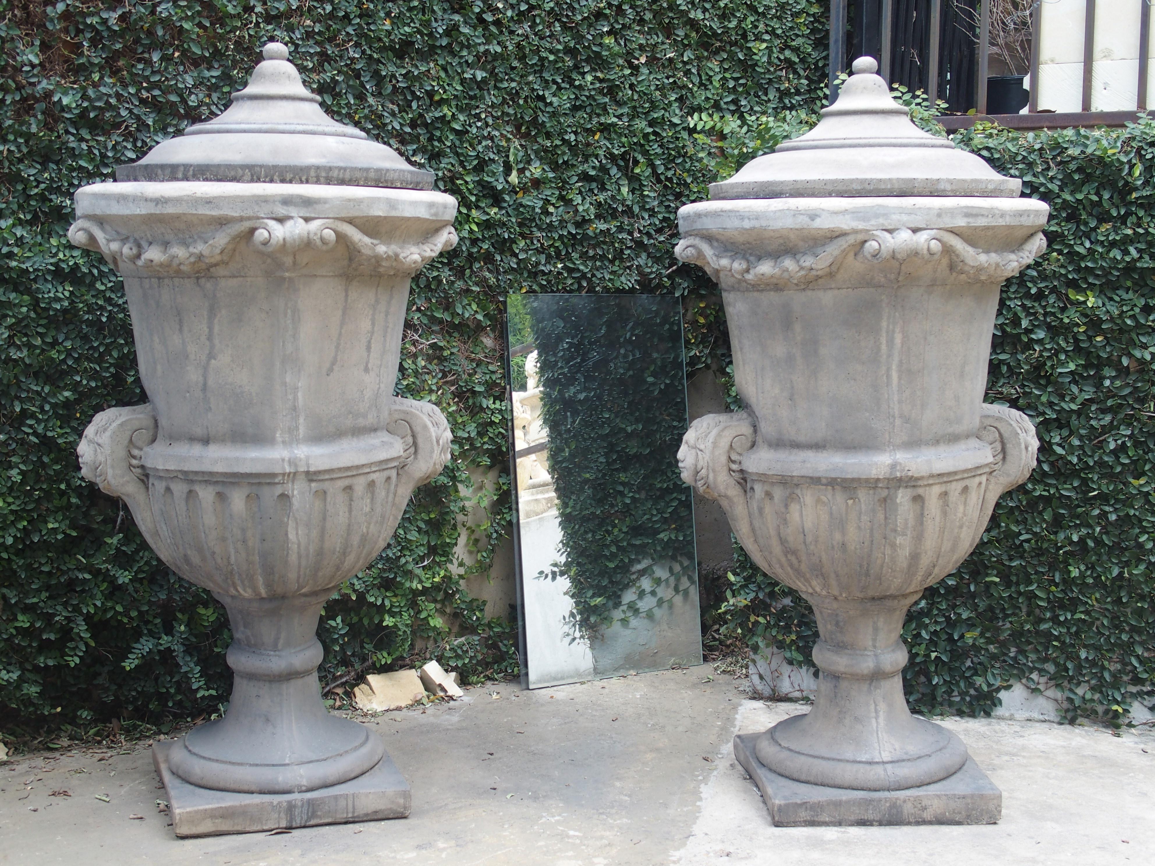 These tall cast stone garden vases from Belgium have lids which allows them to be used as large planters in the summer and garden lidded garden ornaments in the winter. They have swags of fruit and foliation ending in C-Scrolls beneath the lid. On