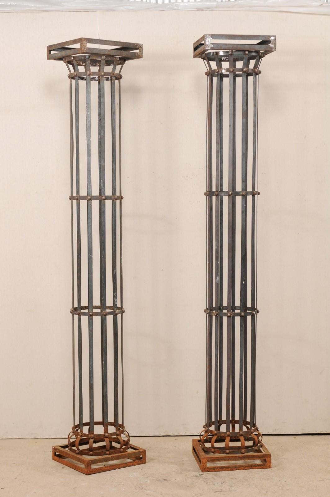 A pair of contemporary American iron architectural columns. This pair of vintage columns feature a round shaped shaft, comprised of vertically set iron strips, with a square-shaped capital and base. Each column standing approximately 8 feet in
