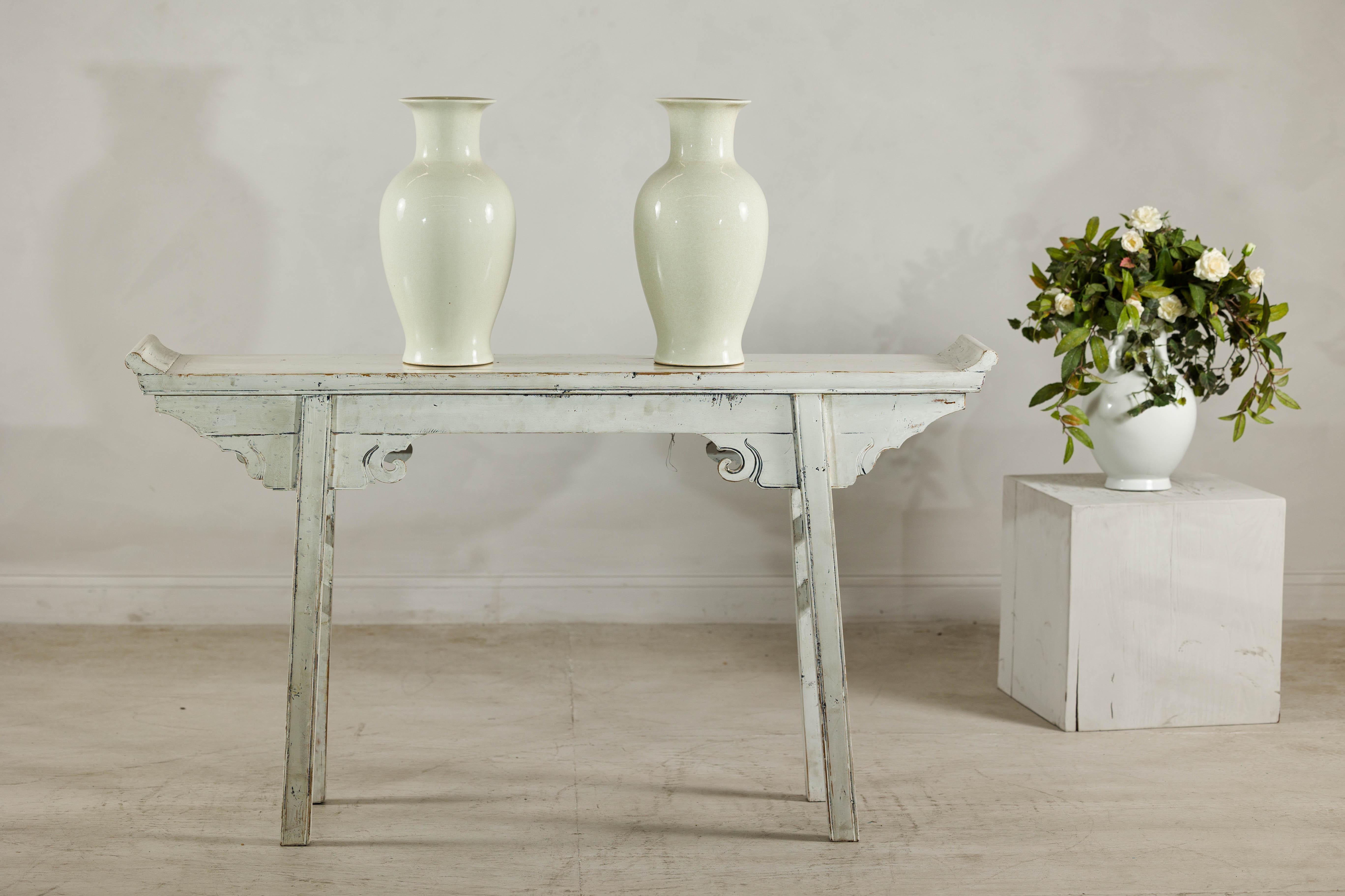 This elegant pair of tall ceramic vases features an understated cream glaze with a fine, allover crackle finish that evokes the timeless beauty of classical Chinese ceramics. Each vase presents a balanced silhouette with a wide flaring rim,