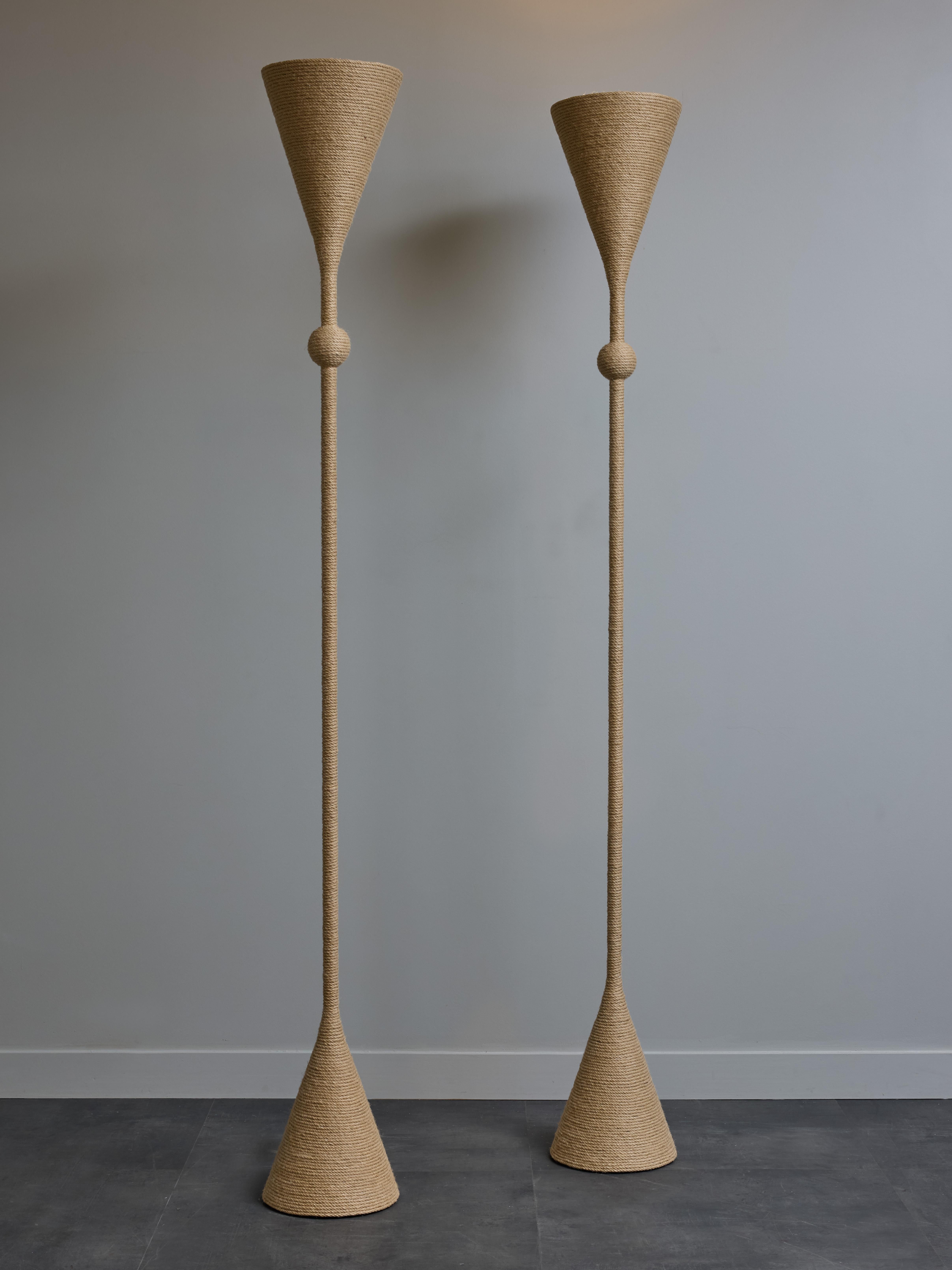 Coppia di lampade da terra alte in metallo interamente avvolte da una corda tesa che gira intorno dai piedi fino alla sommità. 

Una fonte di luce per lampada che, grazie alla forma della parte superiore, fornisce una luce direzionale verso il