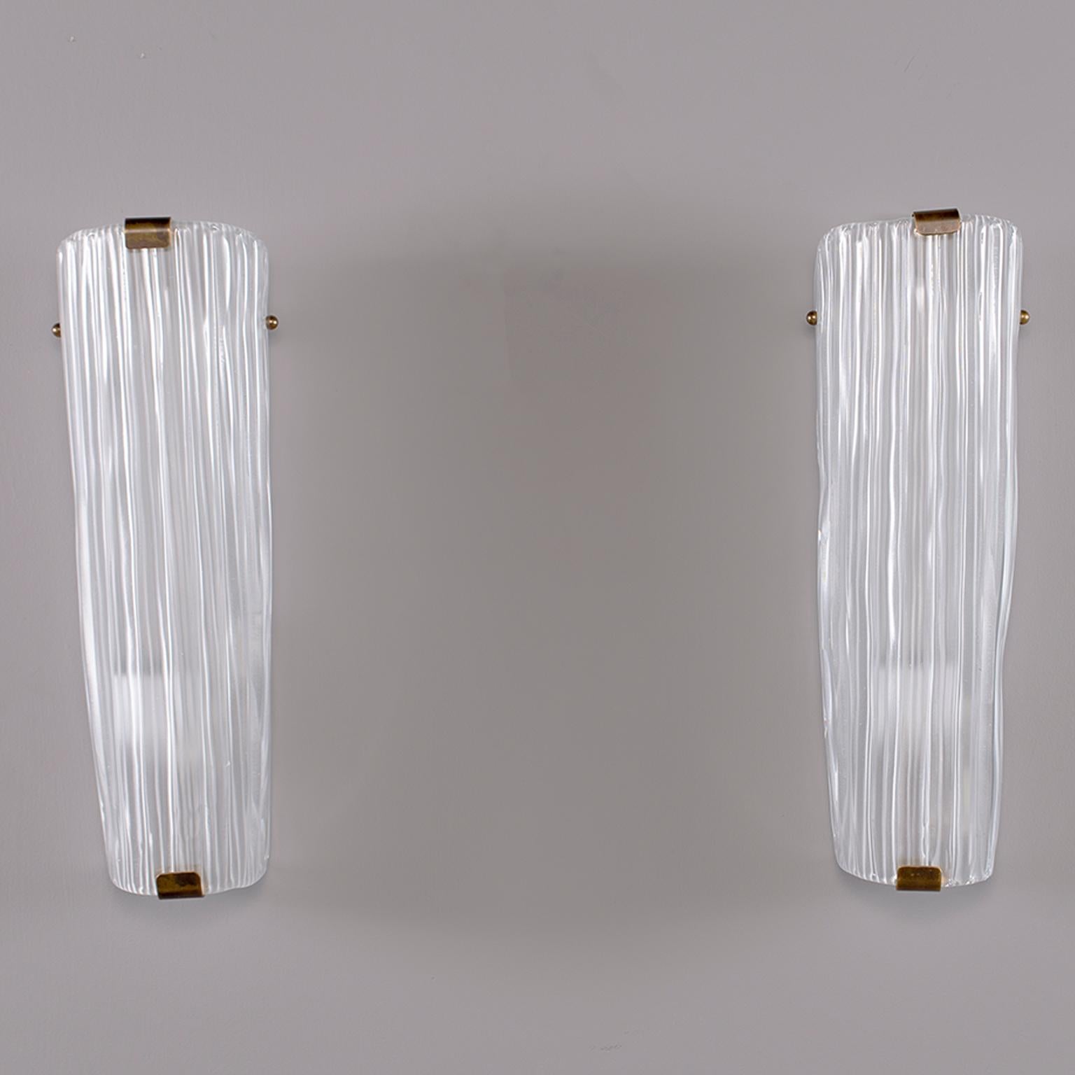 Murano glass sconces are tall and narrow with a ridged or fluted surface and flare slightly wider at the top, circa 1970s. Brass hardware have one full sized socket. Rewired for US electrical standards.