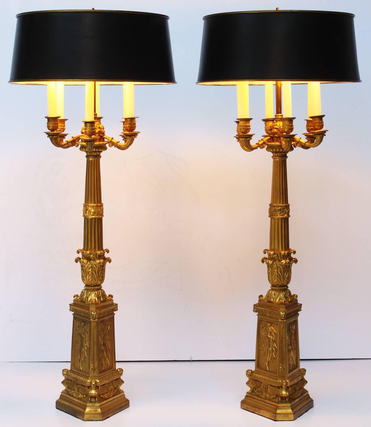 A large pair of French Empire period chased, gilded bronze six-arm candelabra converted into table lamps. The bases rise from triangular plinths supporting three winged sphinxes with intermediate garlands; this tier surmounted by three distinct,