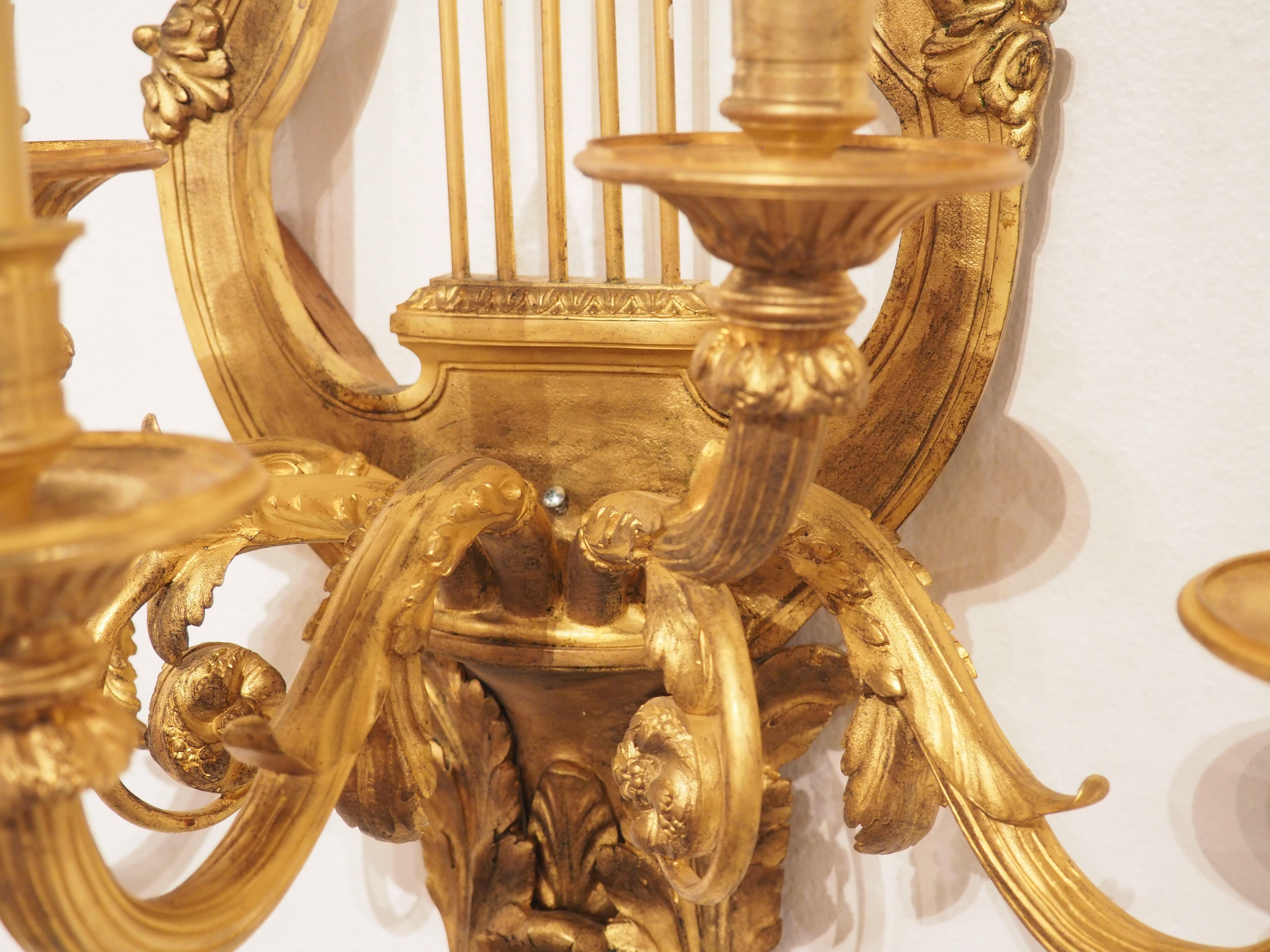 This large pair of wall sconces is made of gilt bronze and dates to the late 19th century.  The design of the sconces is in the Louis XVI taste, as evidenced by the lyre-form body, tied bows, and elegant proportions.  In France, during the reign of