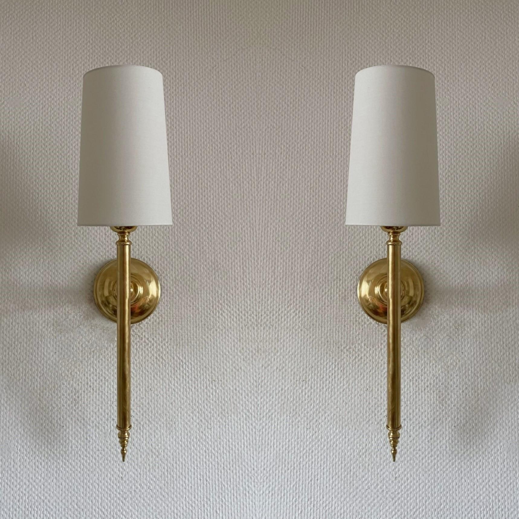 A pair of tall Art Deco torchiere wall sconces in the style of Maison Jansen, France, 1955-1959. Very elegant design made of brass with conical off-white linen shades. Each sconce takes one Edison E27 candelabra screw bulb up to 60watt. LED bulbs