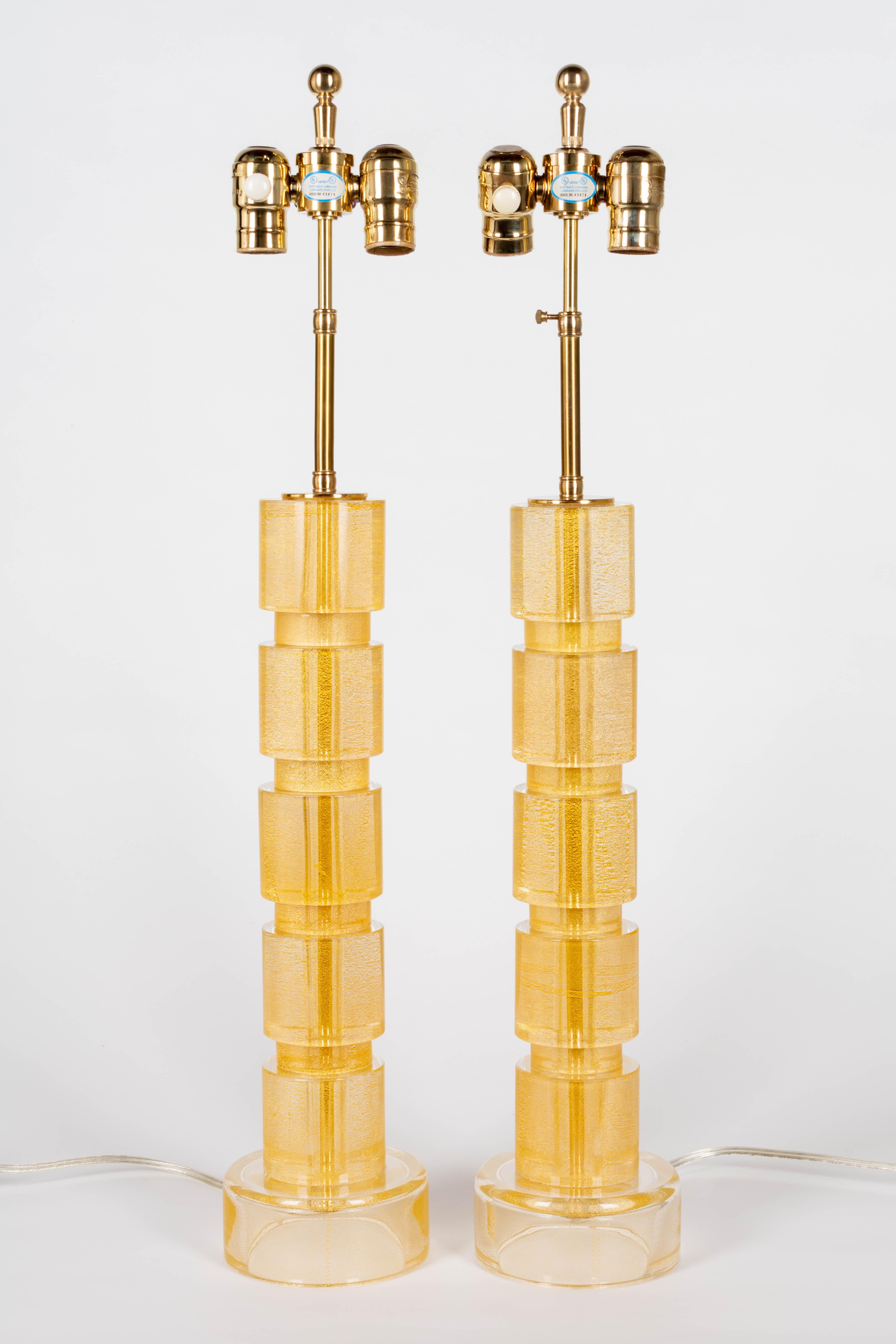 A pair of tall Murano glass column lamps comprised of five solid glass cylinders with gold inclusions. Original high quality polished brass adjustable height, pivoting double cluster sockets with dimmer switches. Shades are not included but measure