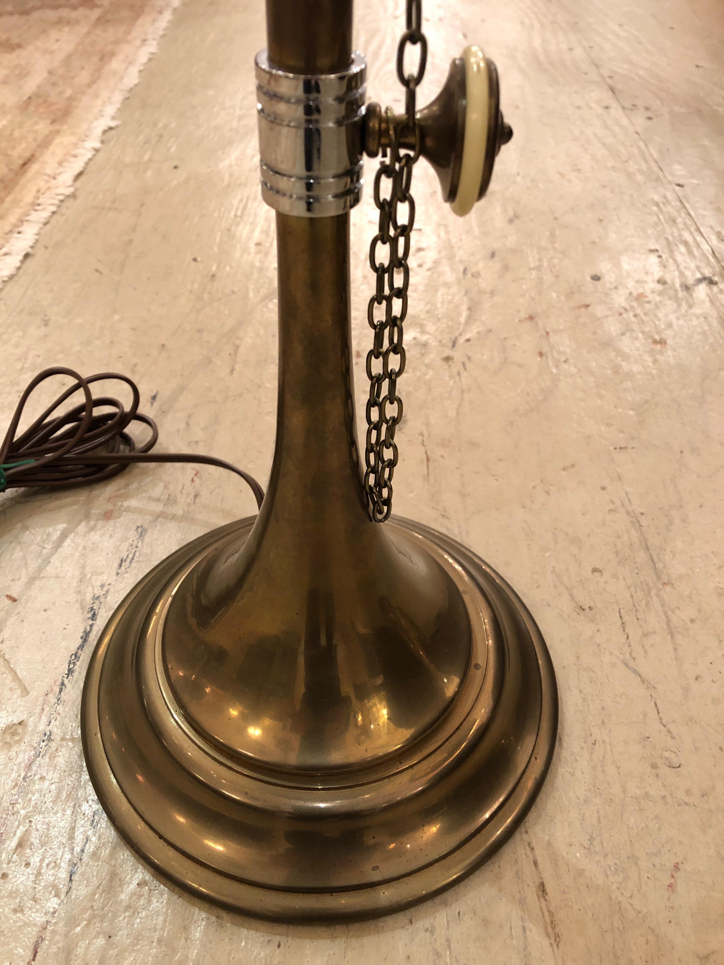A wonderful elongated pair of brass table lamps inspired by musical horns having white enamel knobs, decorative chains, as well as handsome green shades lined in gold.