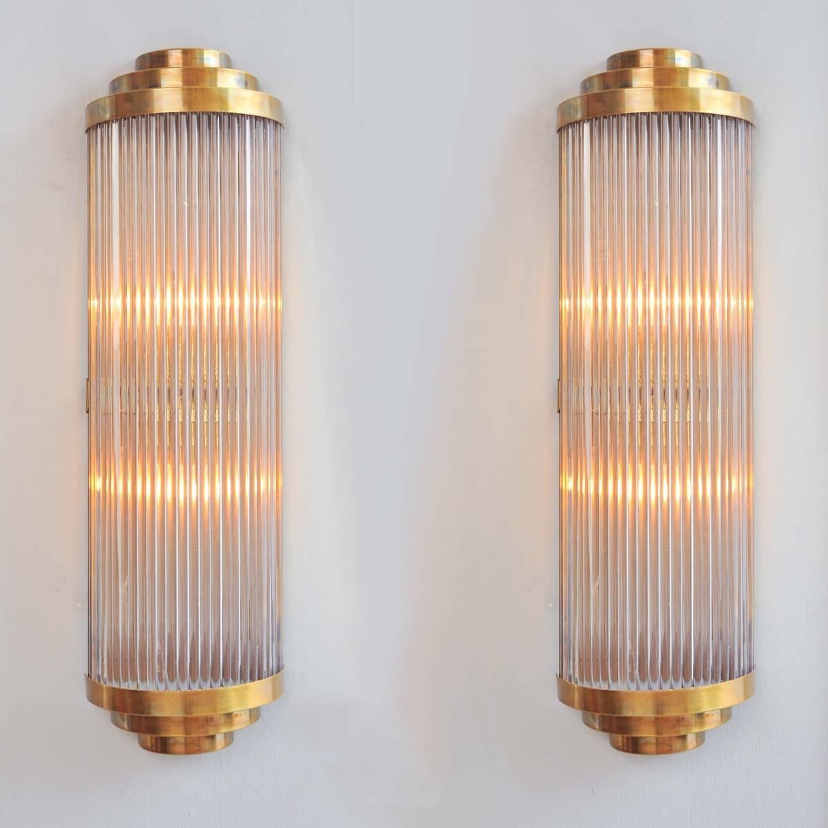 This ‘Ravello’ wall light takes its inspiration from a timelessly classic Art Deco design.
Multiple Italian glass rods form a semi-circle which is capped, top and bottom by 3 tiers of curved brass. The brass back plate holds two light bulbs and
